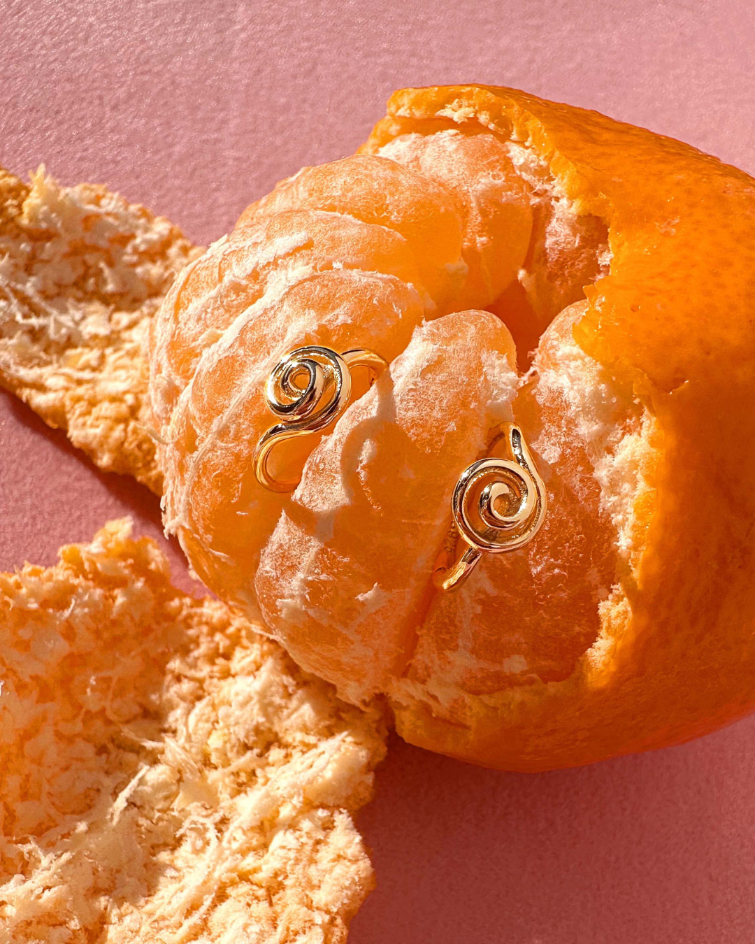 Gold Spiral Huggie Hoops on a mandarin orange
