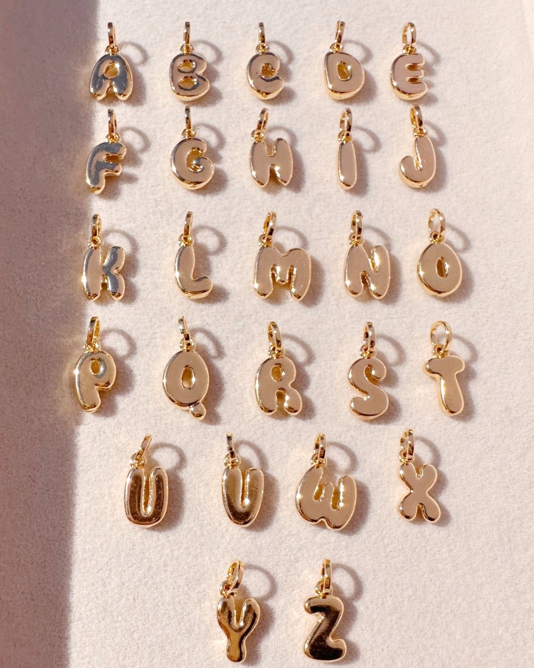 Gold bubble initial letter pendants on a light background