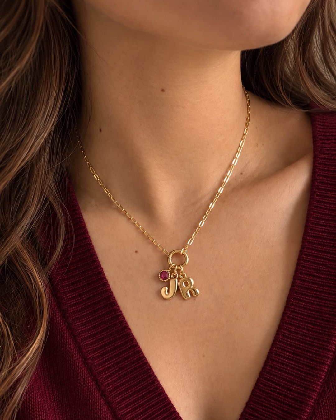 Model wearing the Paperclip Charm Holder Necklace with initial J, R and January Garnet birthstone, in a dark V neck red jumper.