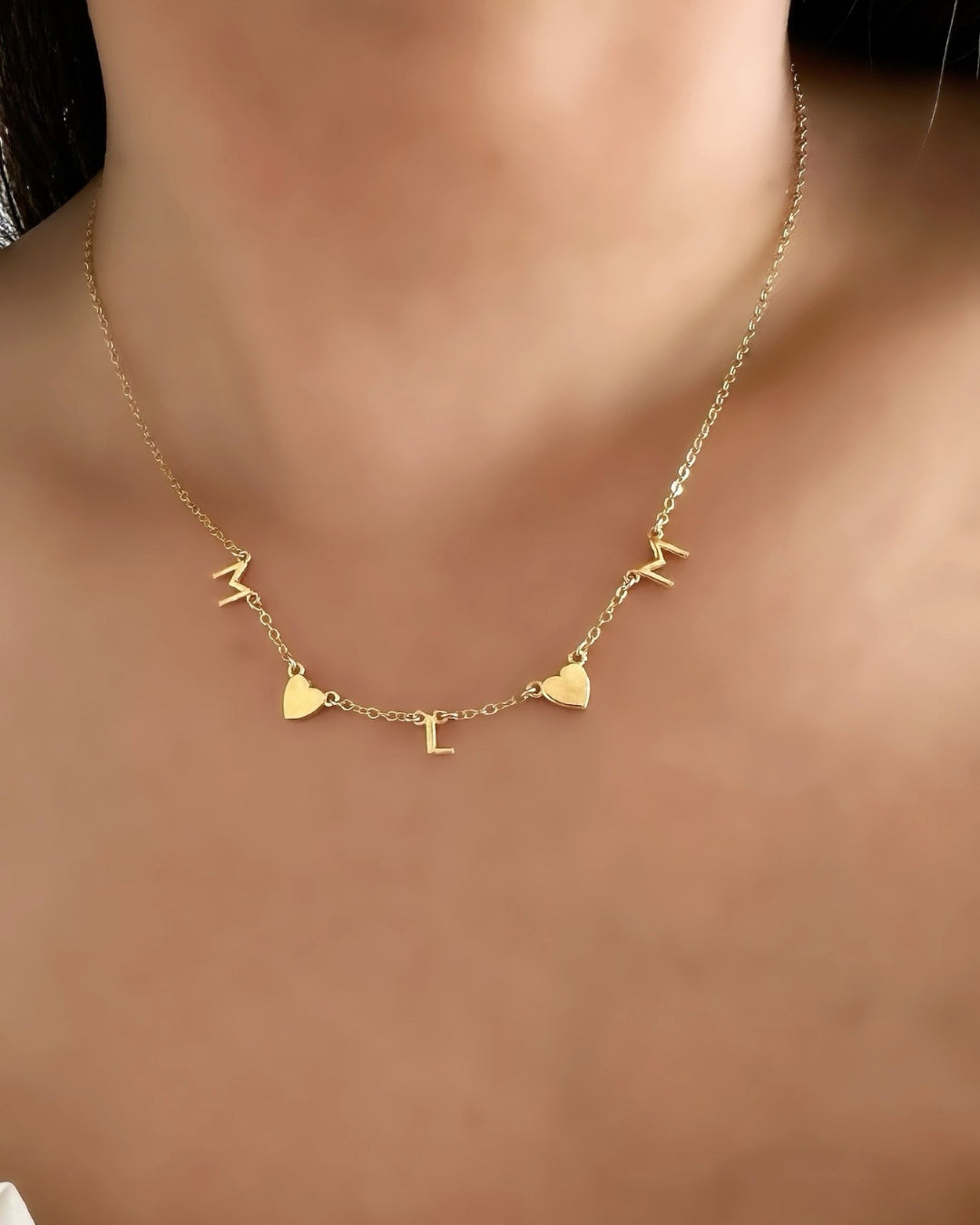 Model wearing Gold-filled necklace with 3 letter charms and 2 gold heart charms evenly spaced on a petite rolo chain.