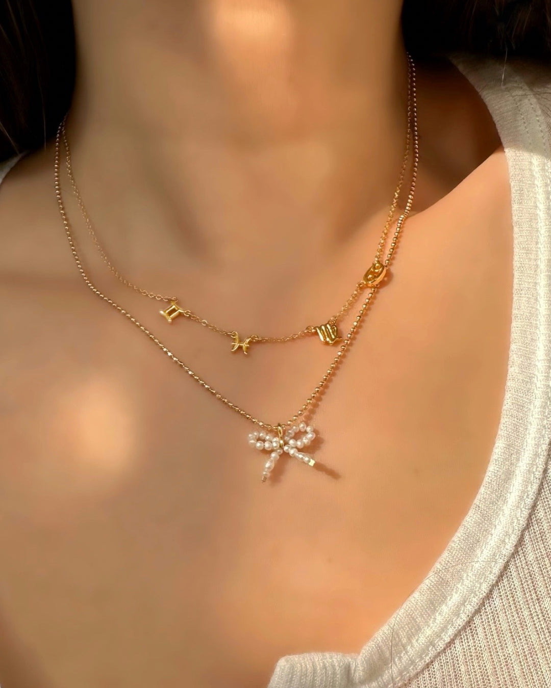 Petite Freshwater Pearl Bow Pendant on a Gold Satellite Chain Necklace layered with a Zodiac Necklace on a model