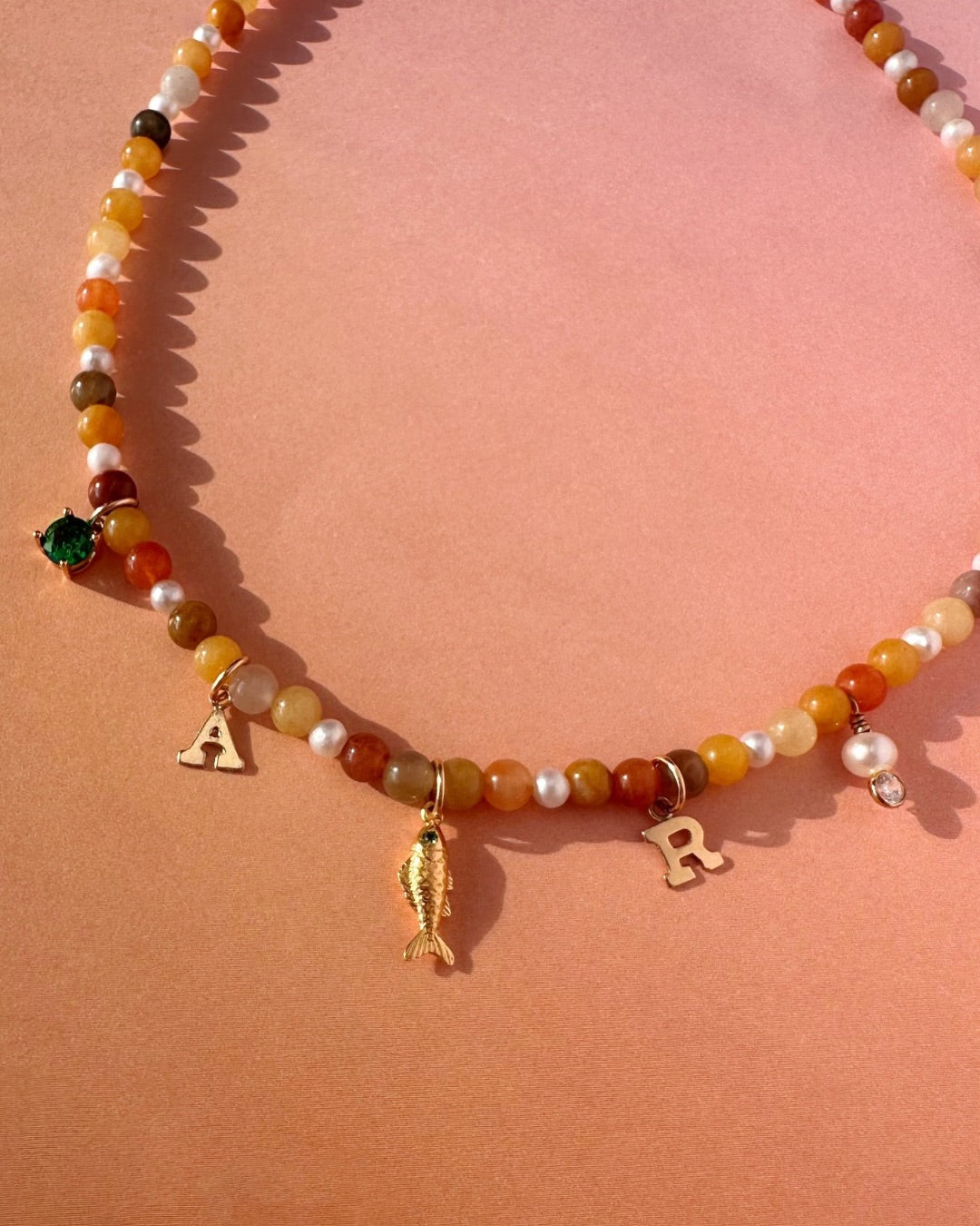 Golden Jade Charm Necklace with gold filled charms on a orange background