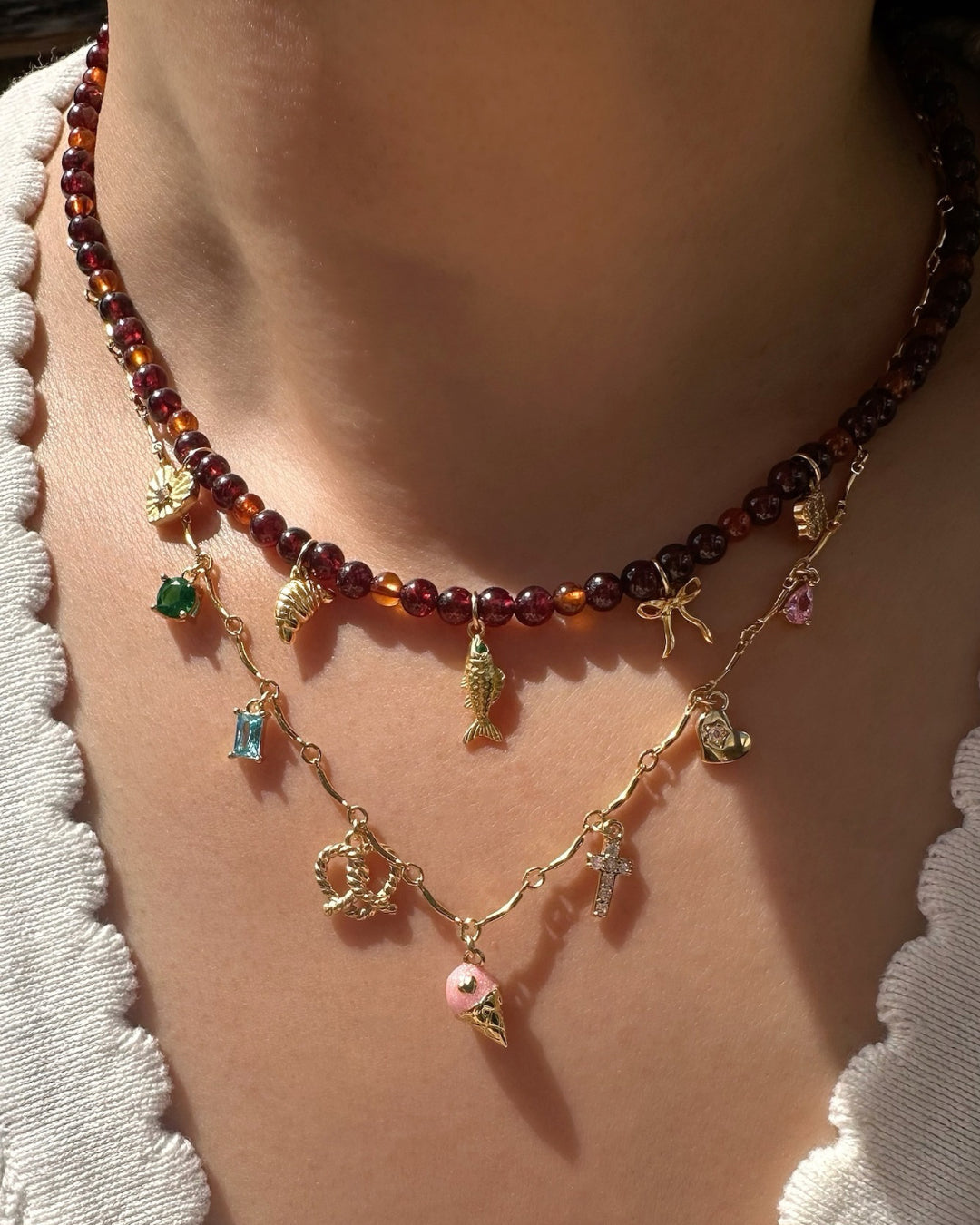 Gold curve bar charm necklace, layered with Garnet Charm Necklace with various charms on a model