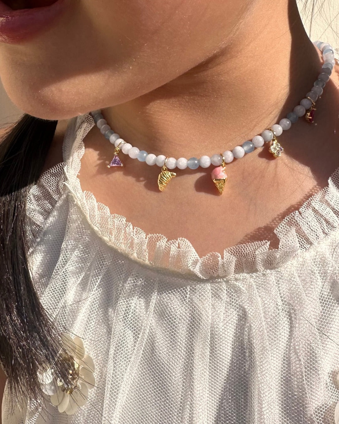 Necklace with aquamarine gemstone charm necklace worn by a person in a white lace top.