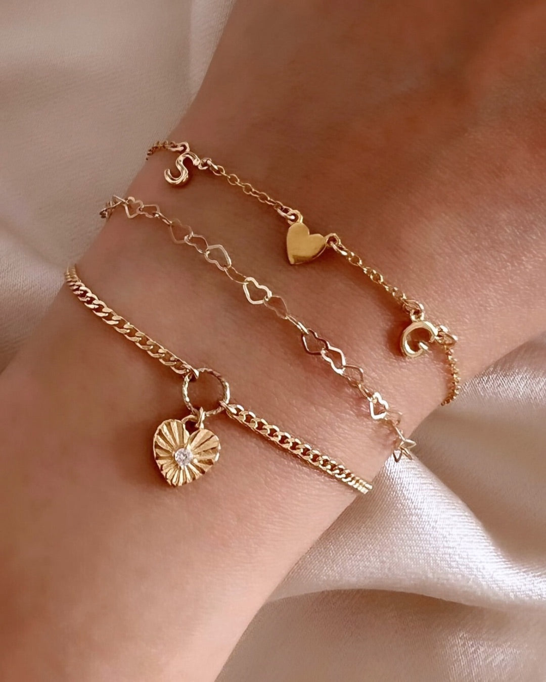Model wearing gold initial bracelet with letter and gold charms on a wrist against a neutral background