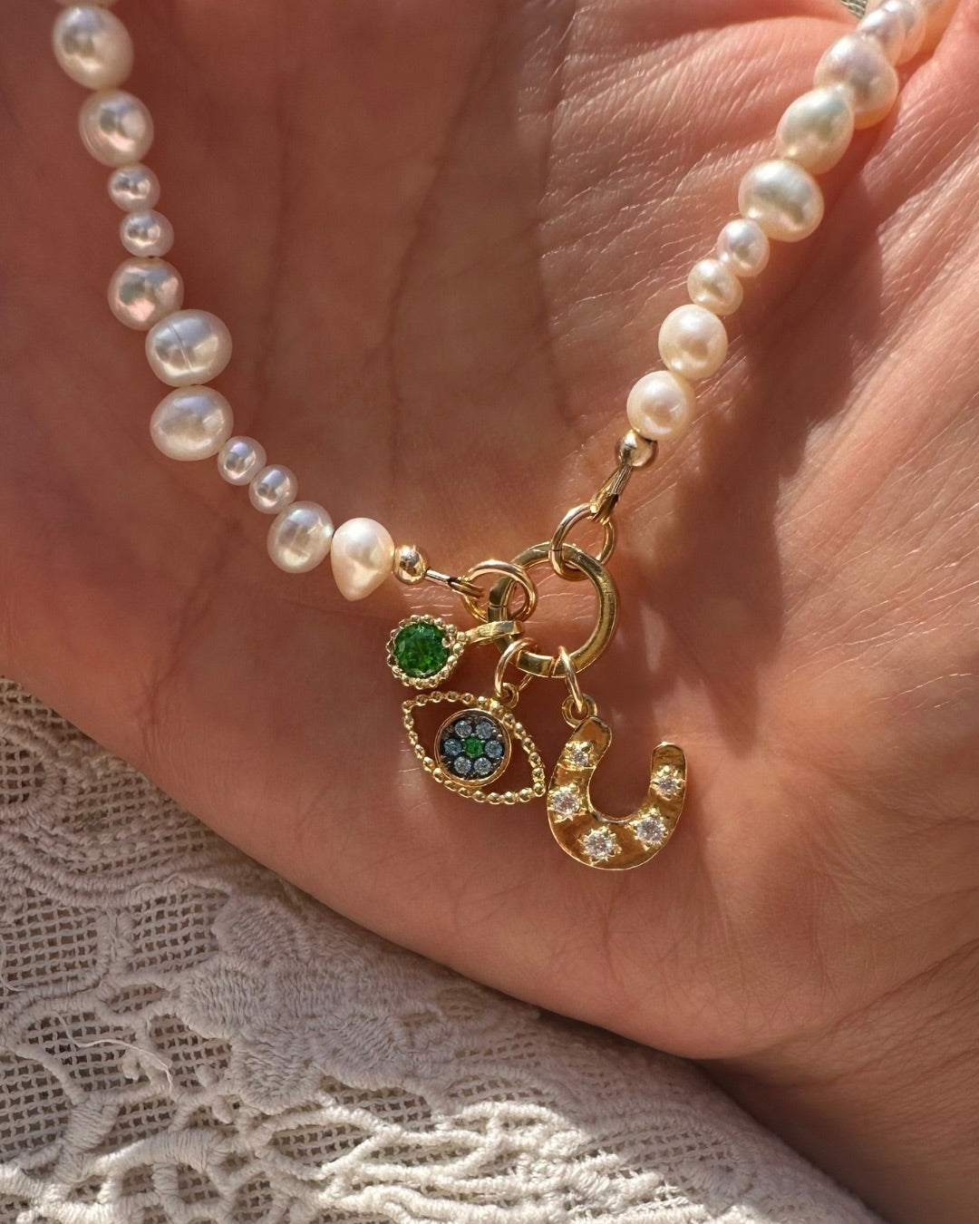 Pearl charm holder necklace with gold charms held in a hand on a textured surface