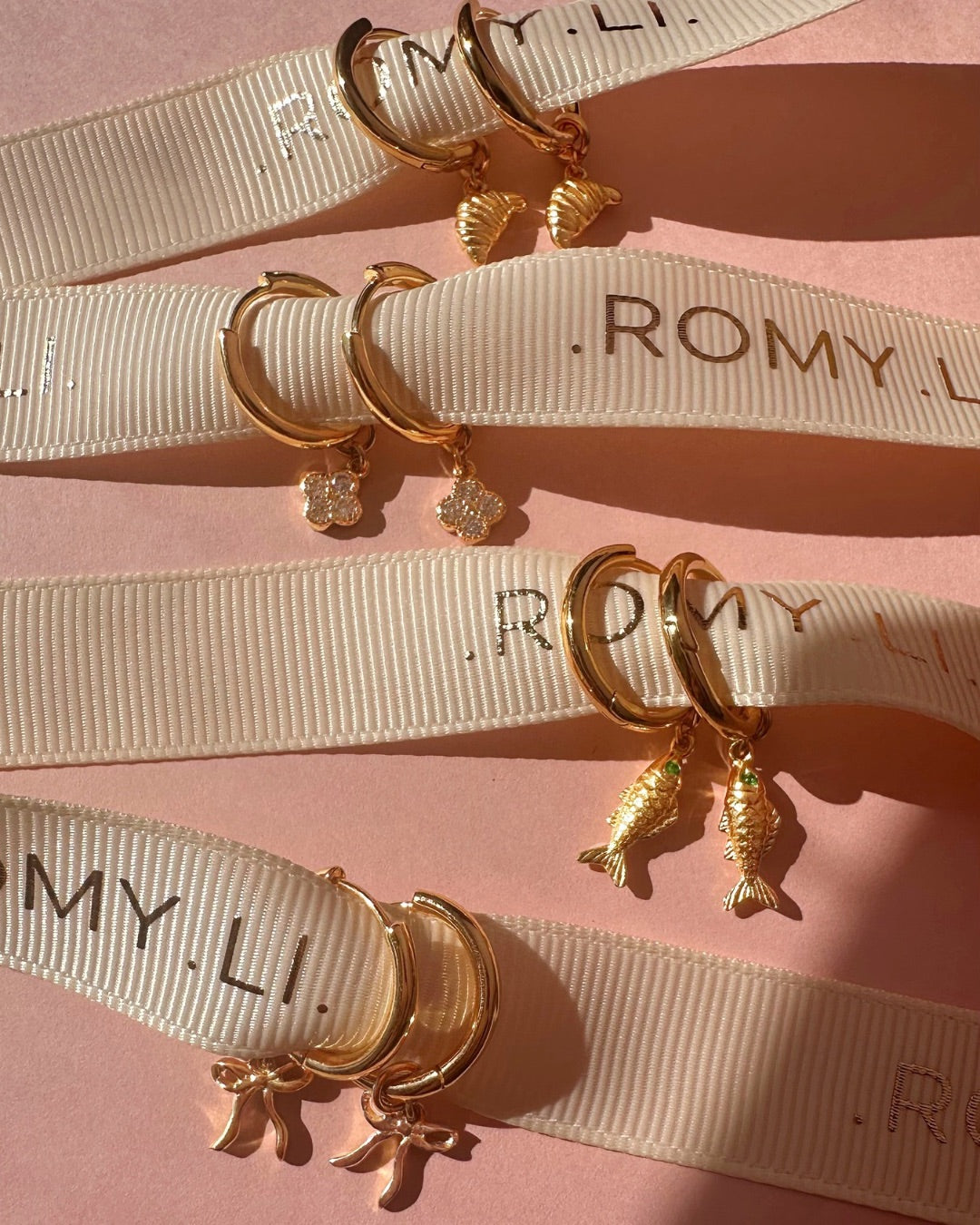 Gold hoop earrings with charms on ribbons with 'ROMYLI ' branding.