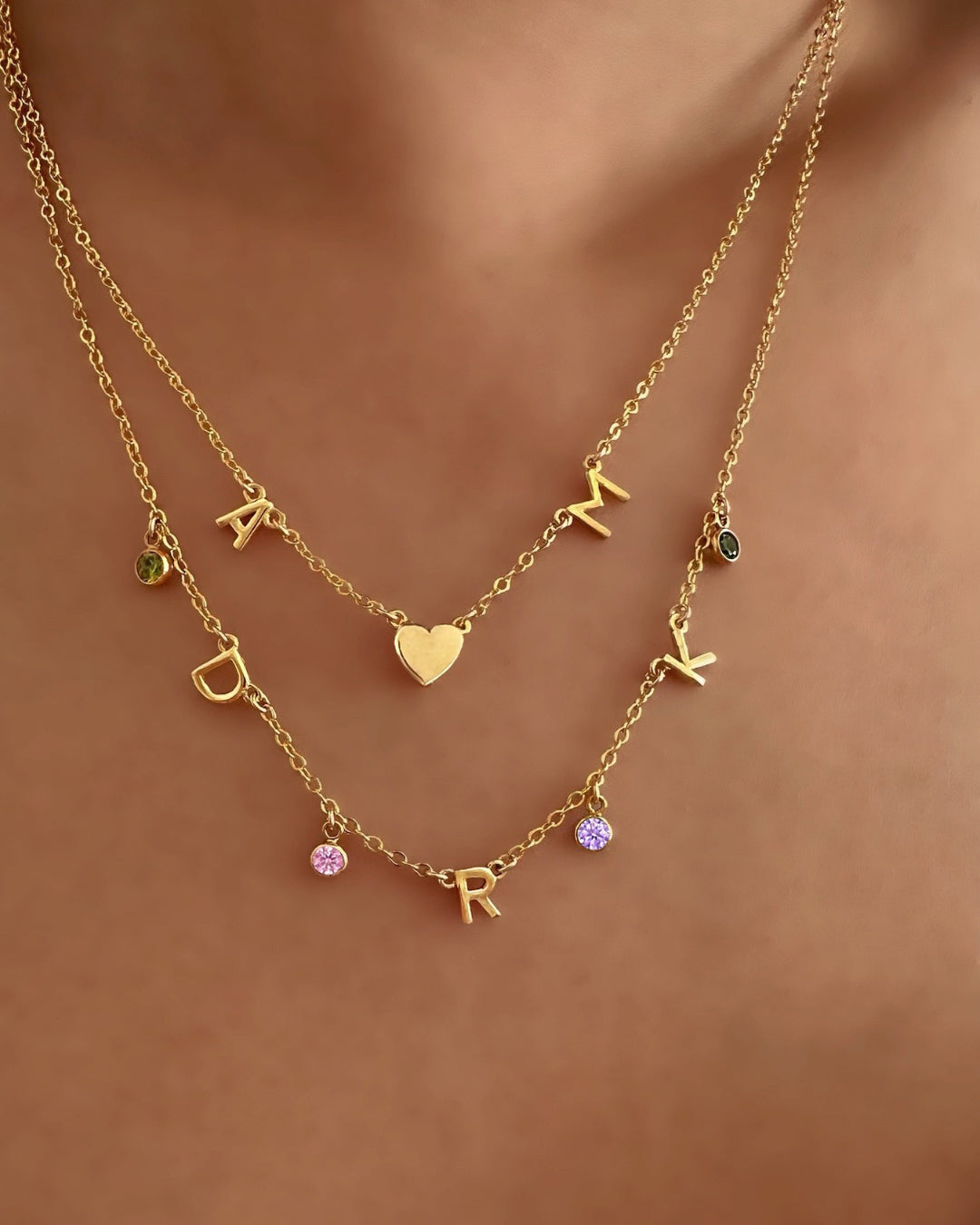 Model wearing gold-filled necklace with 2 letter charms and 1 gold heart charms evenly spaced on a petite rolo chain, and Gold Initial Birthstone Necklace.