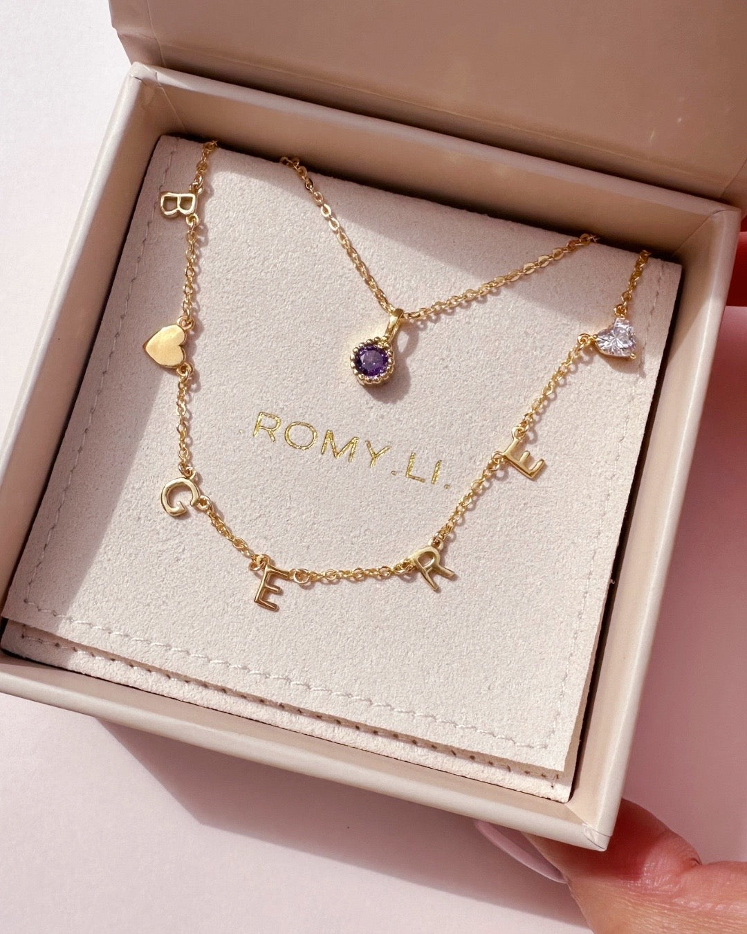 Customisable gold-filled necklace featuring a mix of letter charms, heart gem, and gold heart on a petite rolo chain in a Romyli gift box