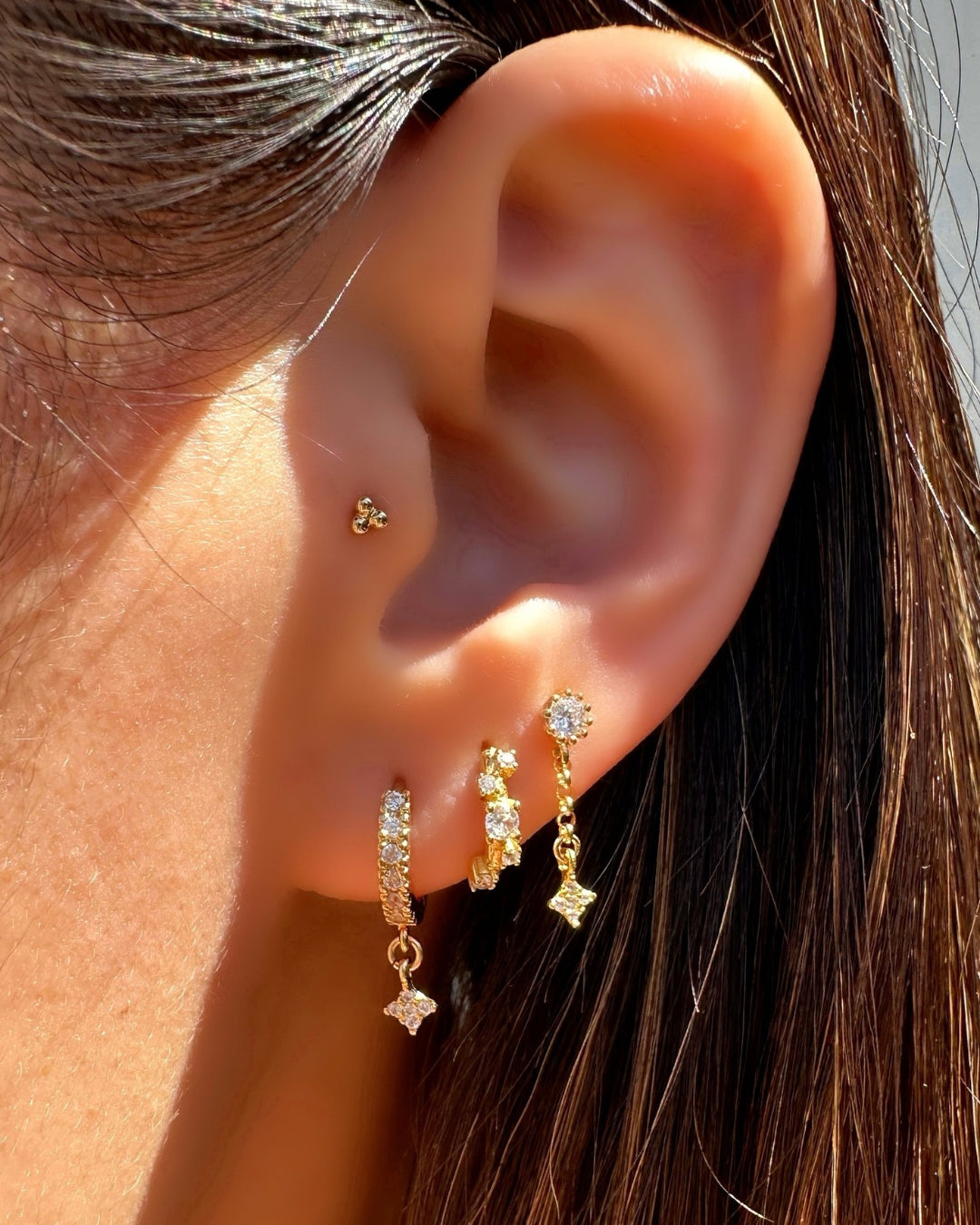 Model wearing gold-colored stack earrings featuring starfall stud earrings, stellar cluster Huggies and gold Starfall charm Huggies.