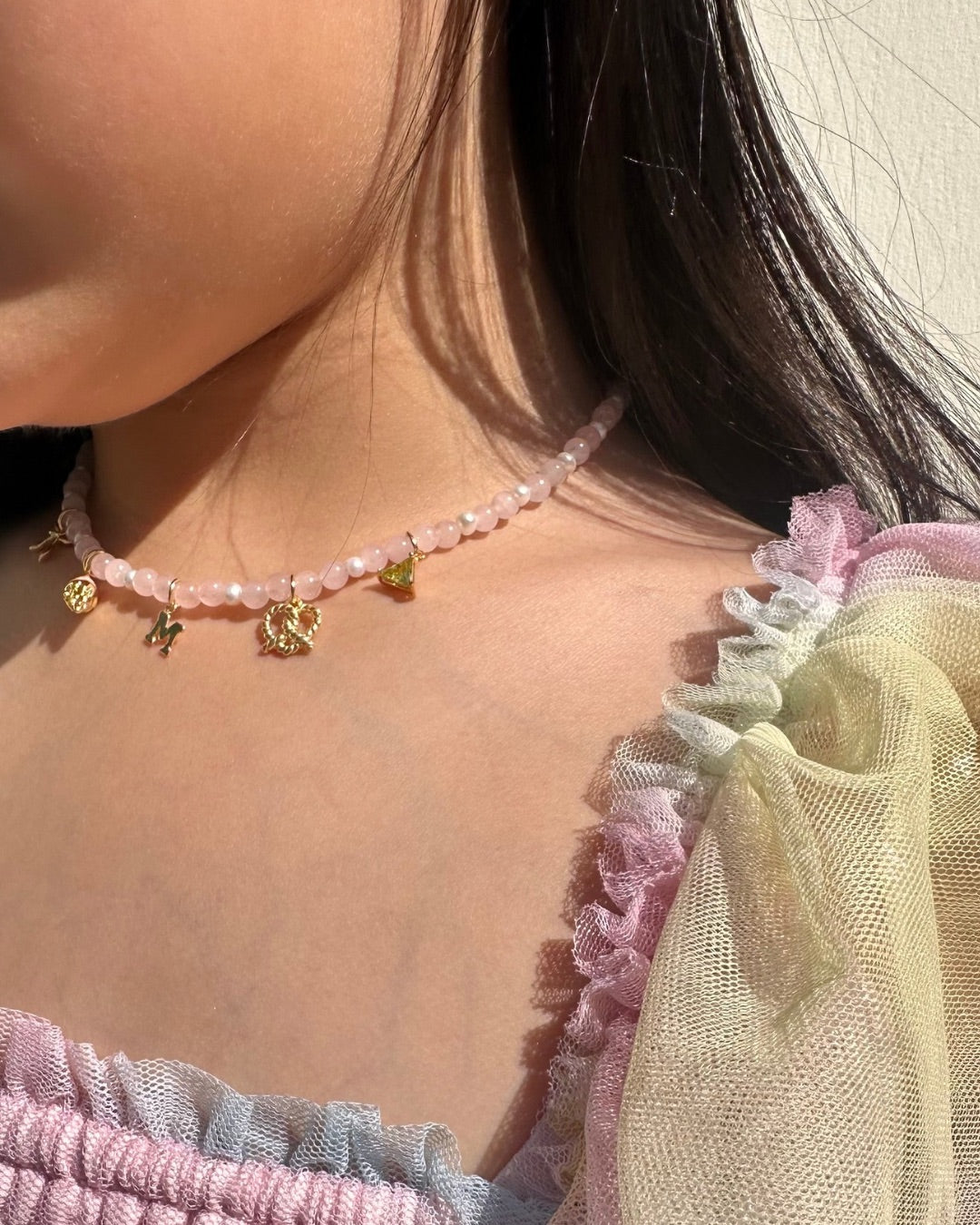 Close-up of a child wearing a delicate pink rose quartz charm necklace with small charms.