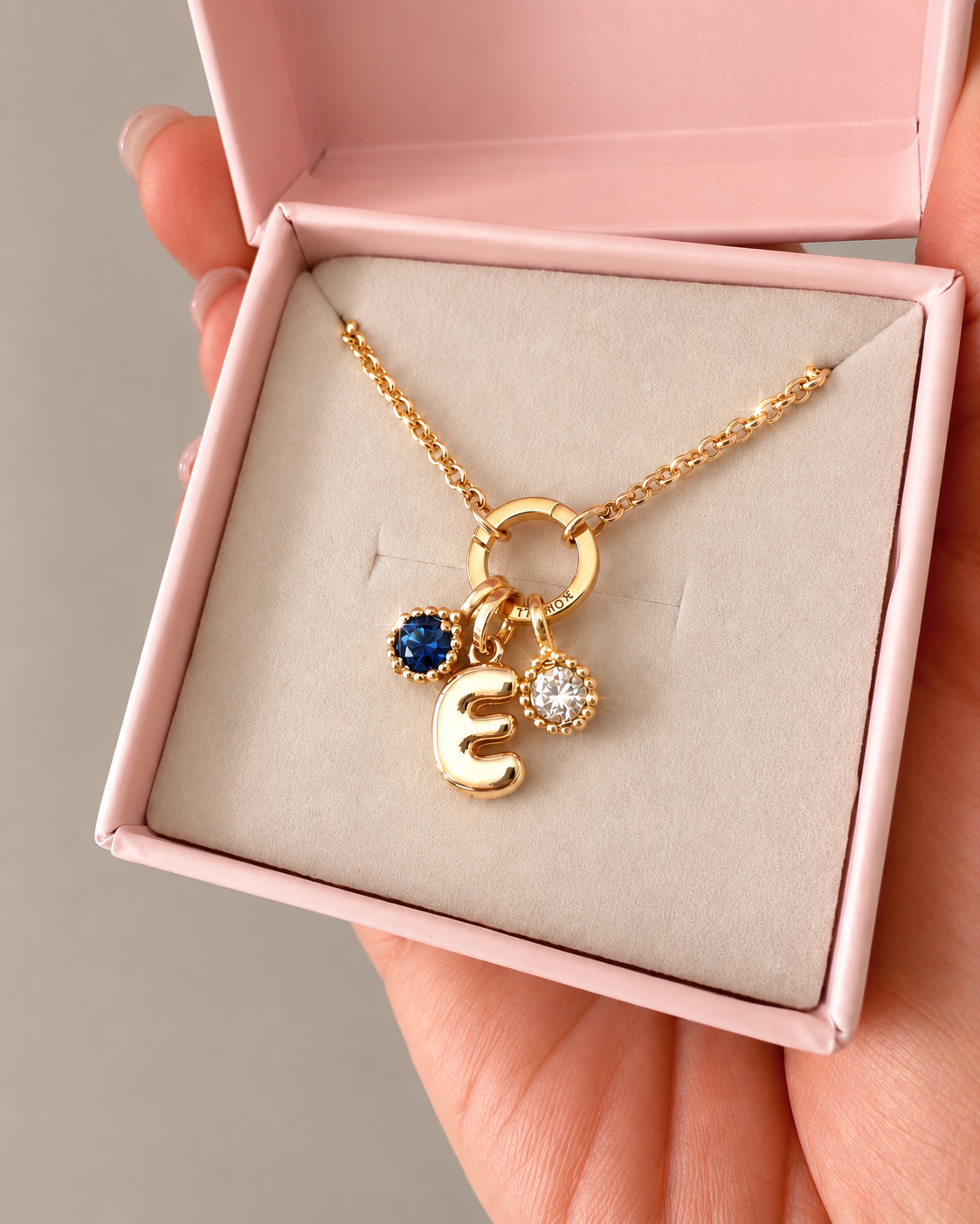 Petit Rolo Charm Holder Necklace with Bubble Initial E and September (Sapphire blue) birthstone and April (Diamond) birthstone in a pink and cream Romyli jewellery box