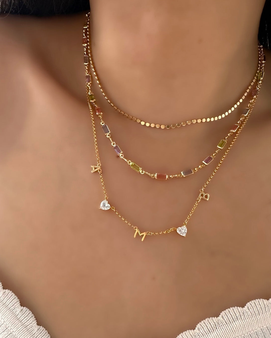 Model wearing gold petite initial necklace, layered with petite Capri necklace and petite snake chain choker.