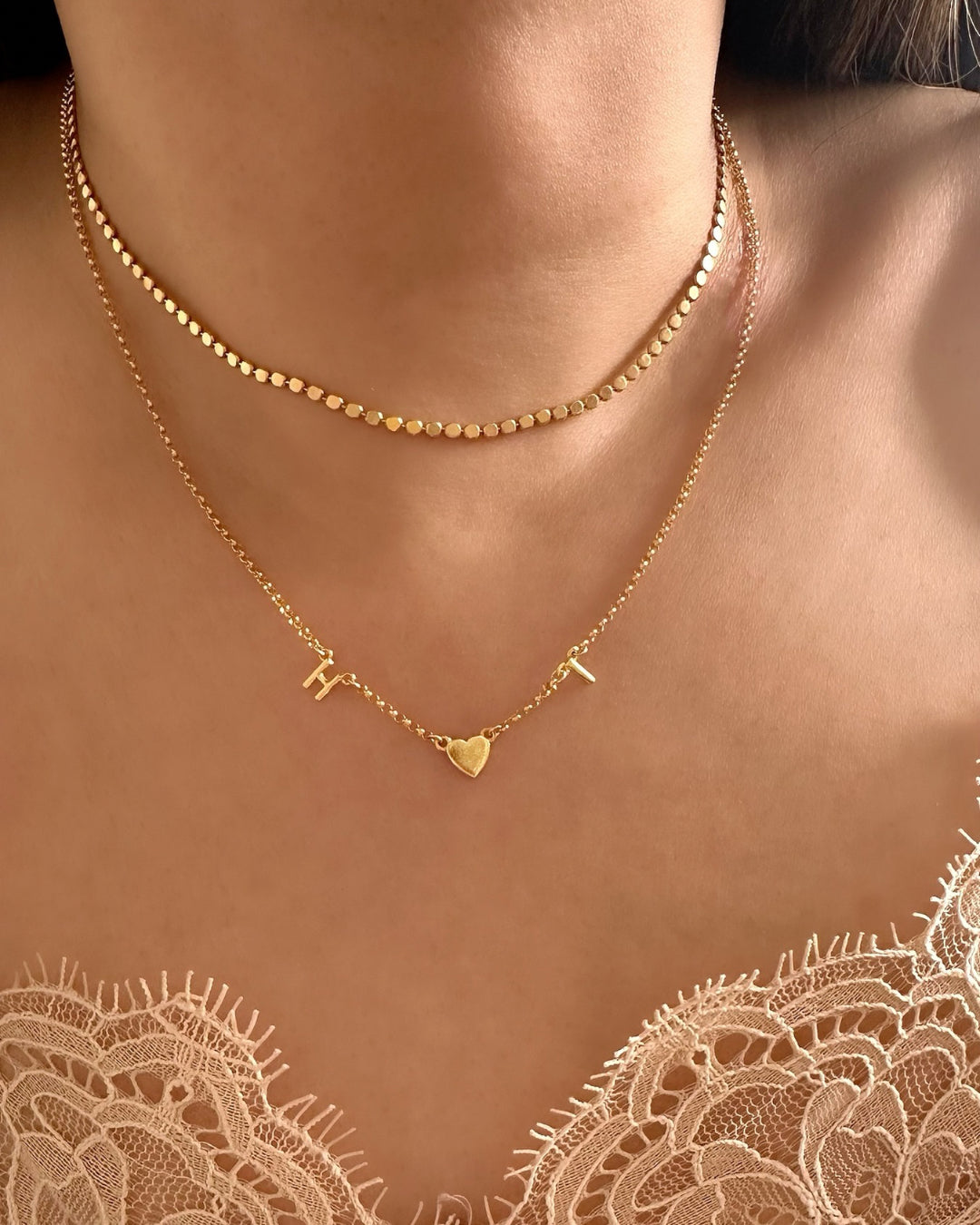 Model wearing gold-filled necklace with 2 letter charms and 1 gold heart charms evenly spaced on a petite rolo chain