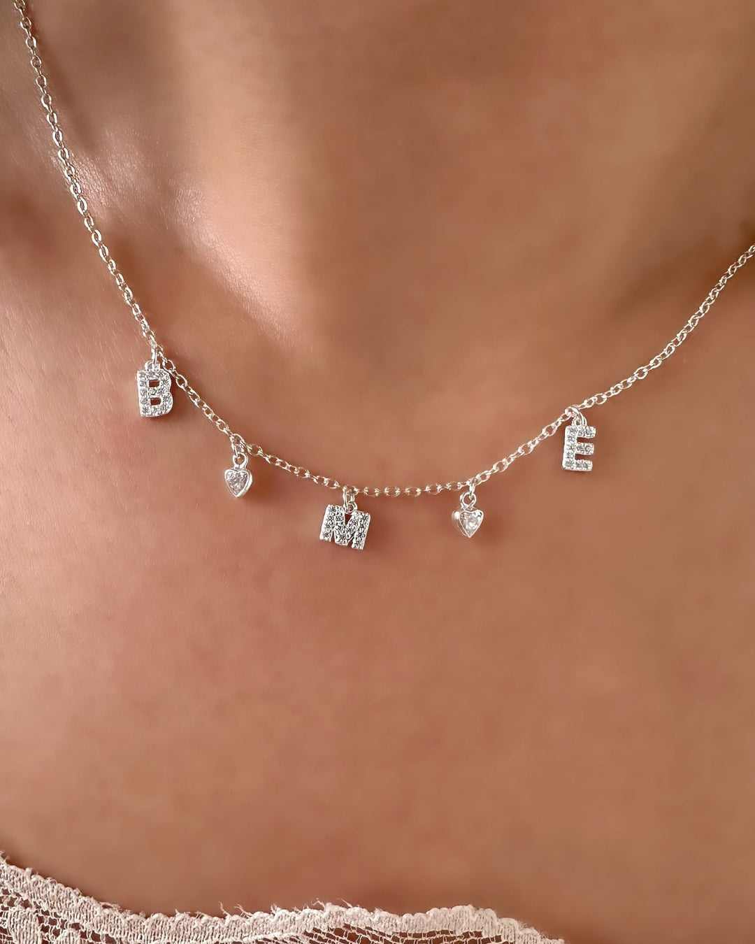 Model wearing silver pavé initial necklace with dainty custom letters and bezel heart charms, personalised sterling silver jewellery for everyday wear