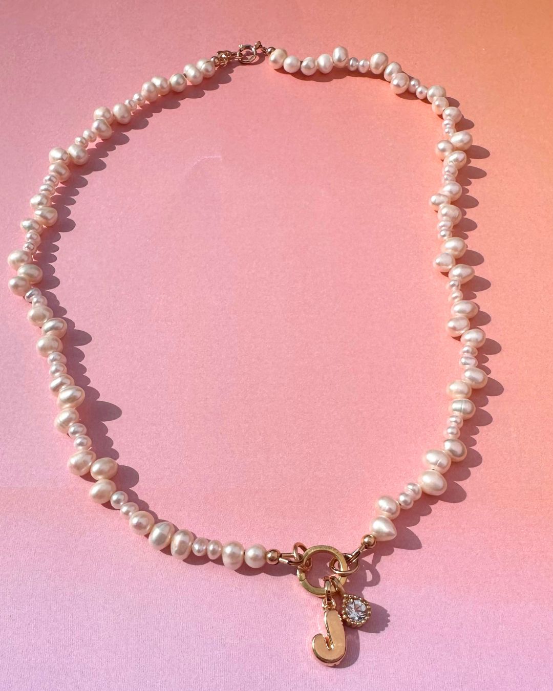 Pearl necklace with a gold charm on a pink gradient background