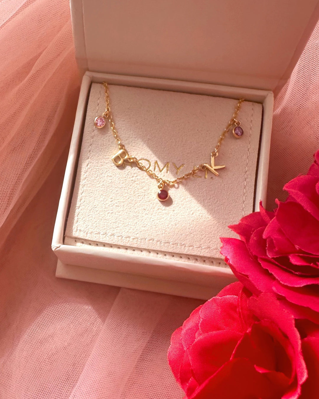 A dainty gold initial birthstone necklace in a gift box, featuring personalized letter and birthstone charms, elegantly displayed on a fine gold chain. Perfect for everyday wear and meaningful gifting.