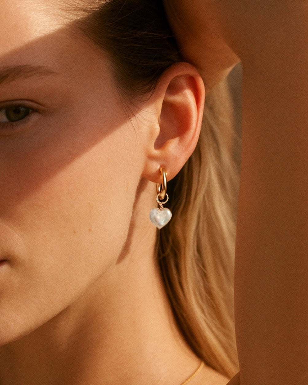 14k yellow gold fill hoops with freshwater pearl heart charm earrings on a model