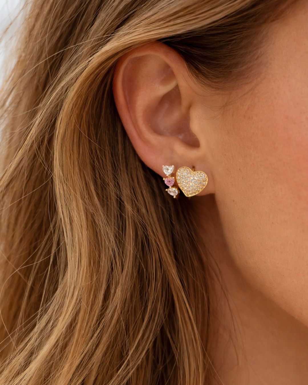 Close-up of an ear wearing a gold heart-shaped earring with pink accents.