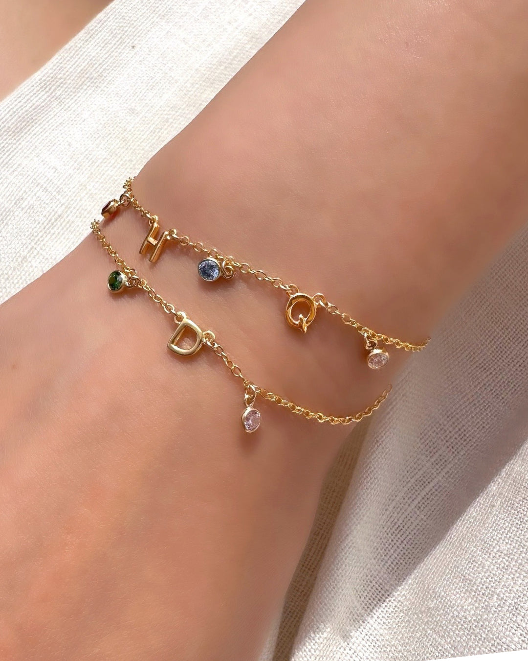 A delicate gold initial birthstone bracelet on a model, customisable with up to 9 initials and birthstones, elegantly set on a fine gold chain. A timeless and meaningful piece for everyday wear and gifting.