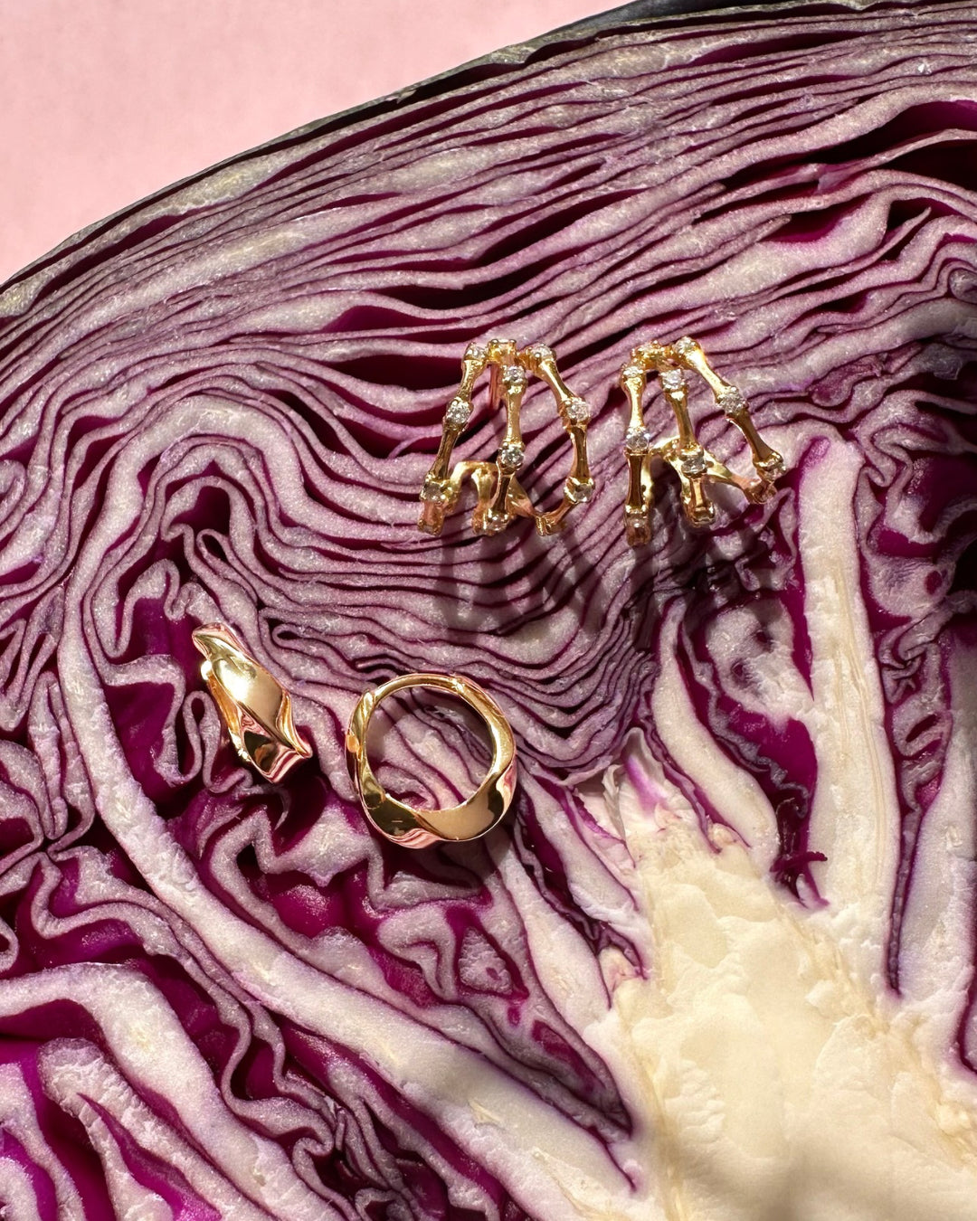 Gold Molten Dome Huggie Hoop earrings and Trellis Pavé Huggies on a sliced red cabbage with a pink background