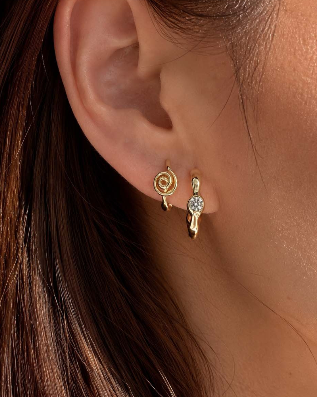 Woman wearing gold sculpted hoop and gold spiral Huggie hoops