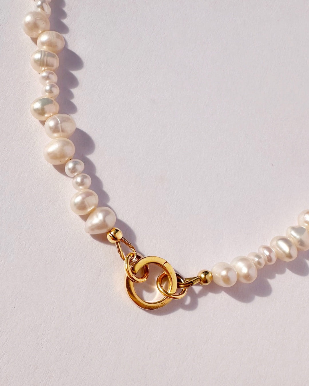 Close up of Pearl Pendant Ring necklace with a gold clasp on a light gray background