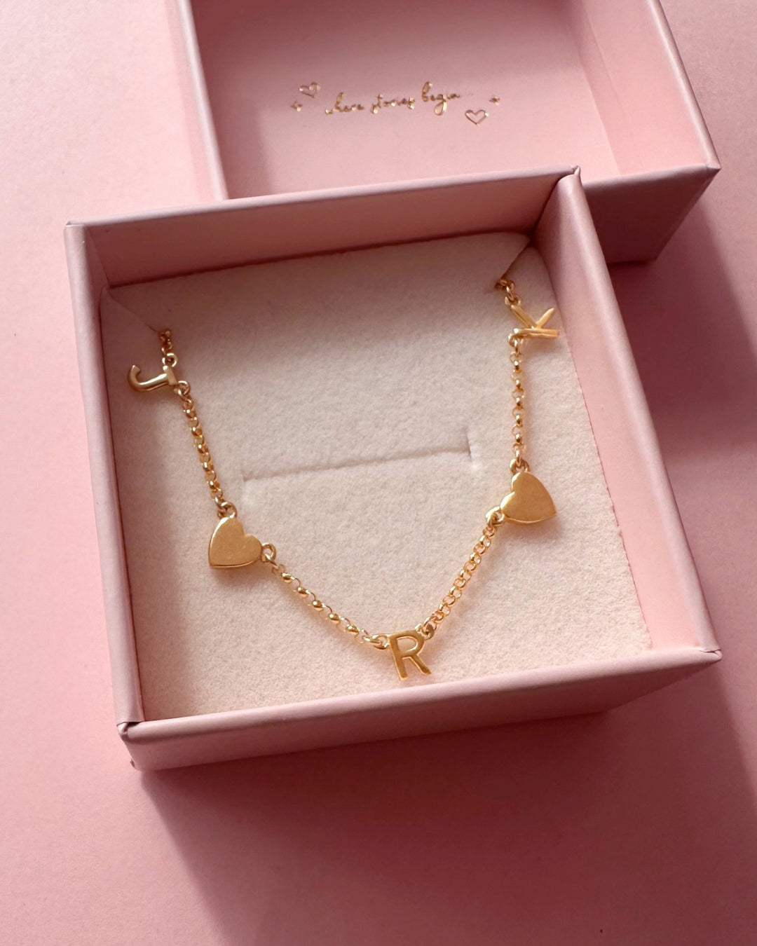 Gold-filled necklace with 3 letter charms and 2 gold heart charms evenly spaced on a petite rolo chain in a Romyli gift box.