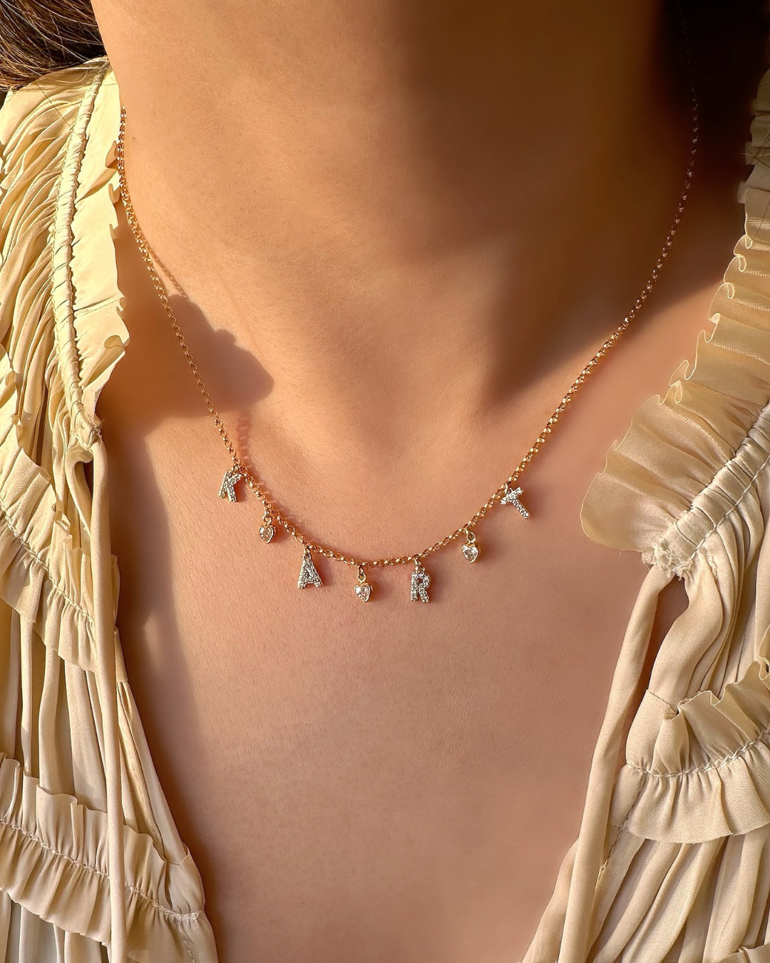Model wearing layered gold pave initial necklaces with personalised letters and tiny bezel heart charms, dainty gold jewellery for everyday wear