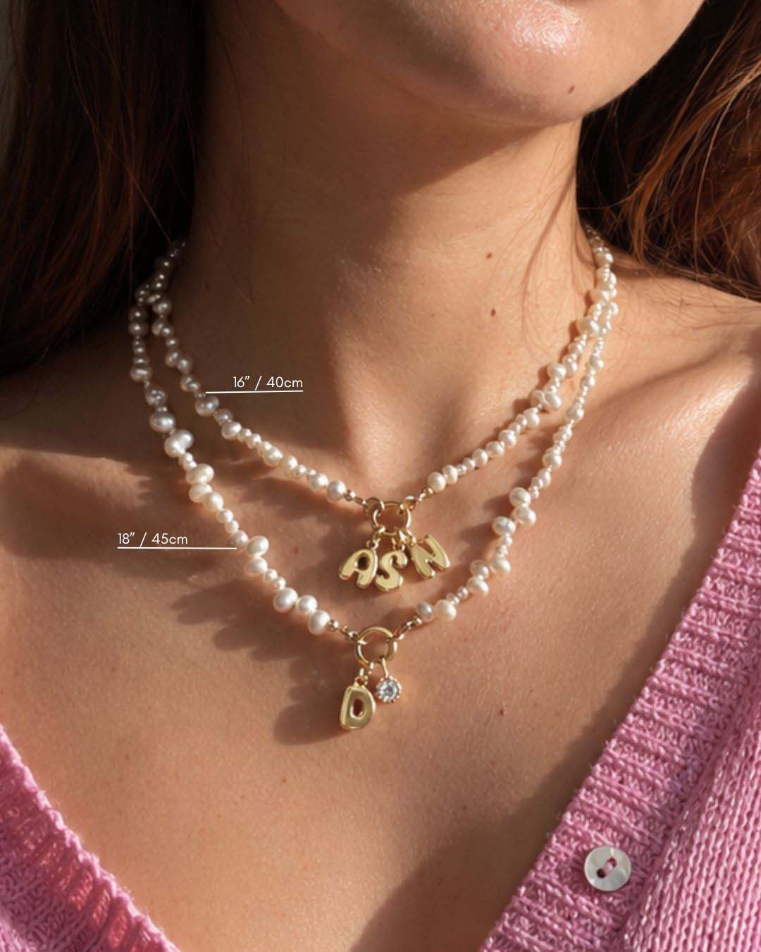 Close-up of a woman wearing a 16” (40cm) and 18” (45cm) pearl charm holder necklace with gold pendants, set against a blurred background.