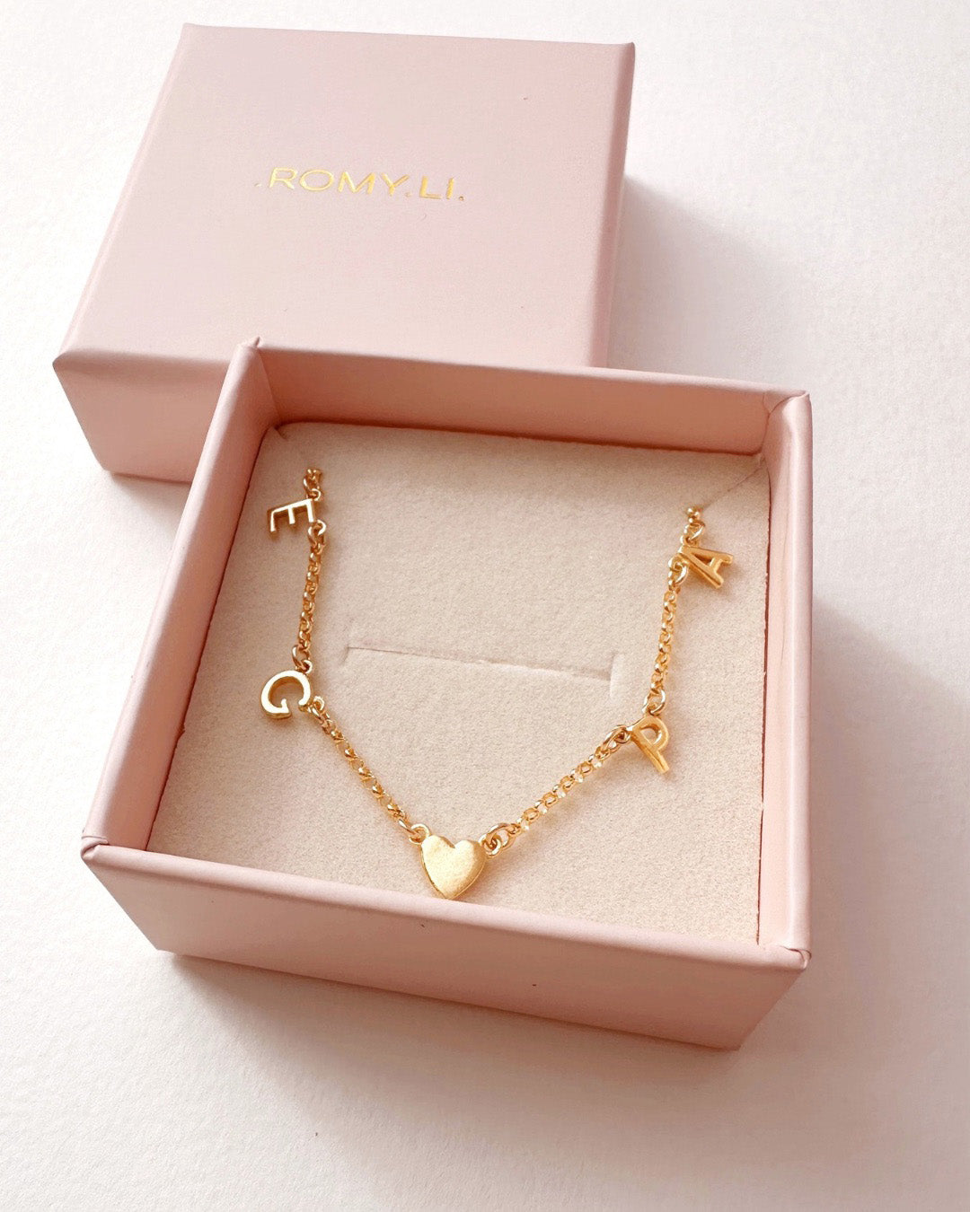 Gold necklace with gold initial letters and heart charm in a pink box