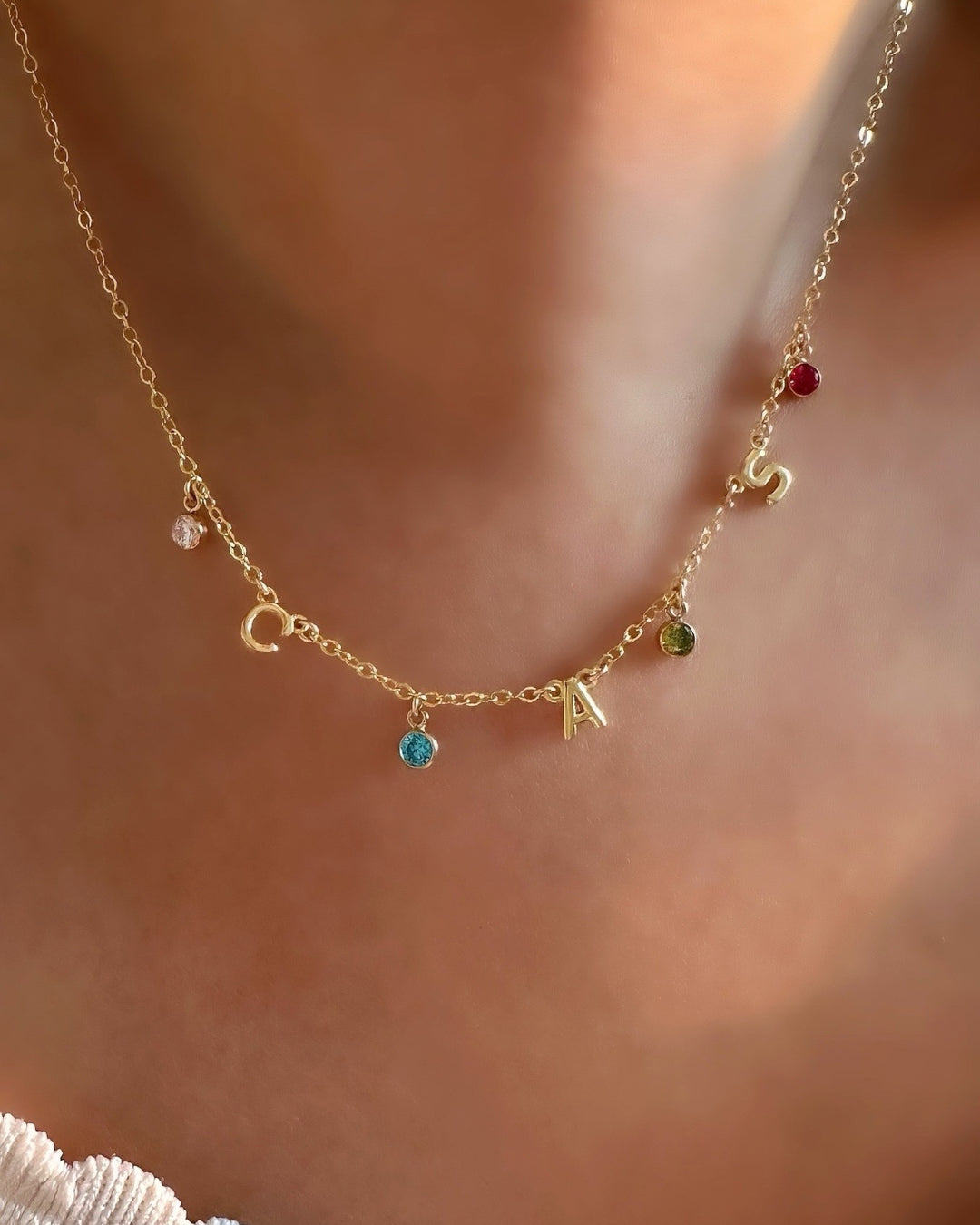 A dainty gold initial birthstone necklace on a model, featuring personalized letter and birthstone charms, elegantly displayed on a fine gold chain. Perfect for everyday wear and meaningful gifting.