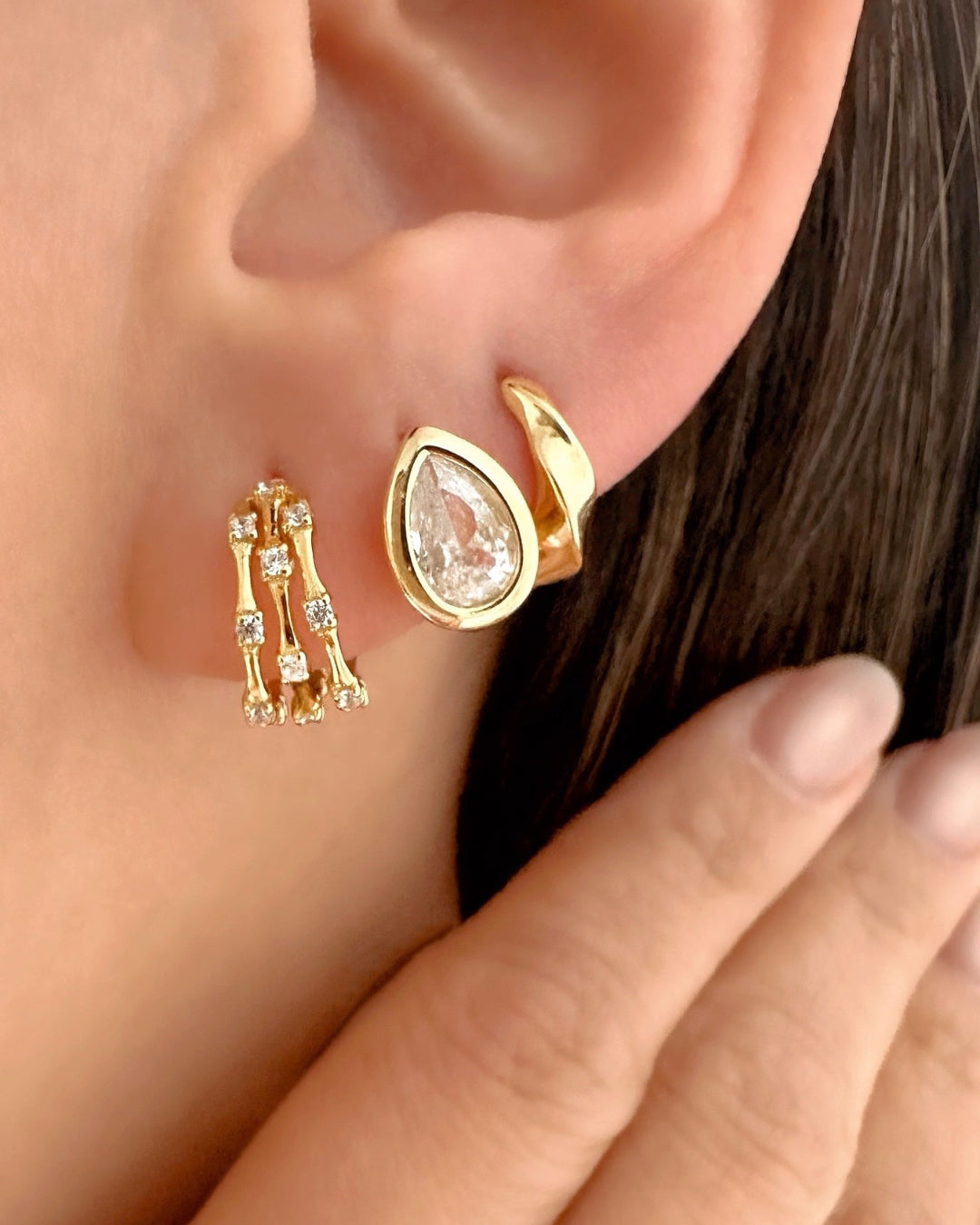 Close-up of gold vermeil huggie ear stack being worn. Featuring the Trellis Pavé Huggies,, Teardrop Bezel Huggies and Molten Dome Huggies.