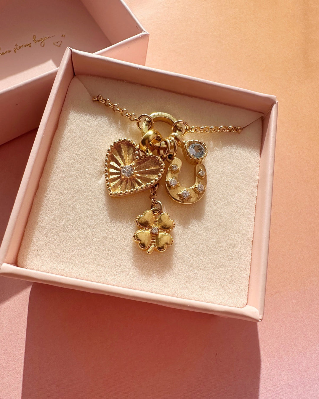 Heart Token Pendant with white cubic zirconia crystal centre, sunray etching, and milgrain detail. Paired with Romyli’s gold Petite Rolo Chain, Clover Pendant, Horseshoe Pendant, and March Aquamarine Birthstone Pendant. All styled inside a Romyli jewellery gift box.