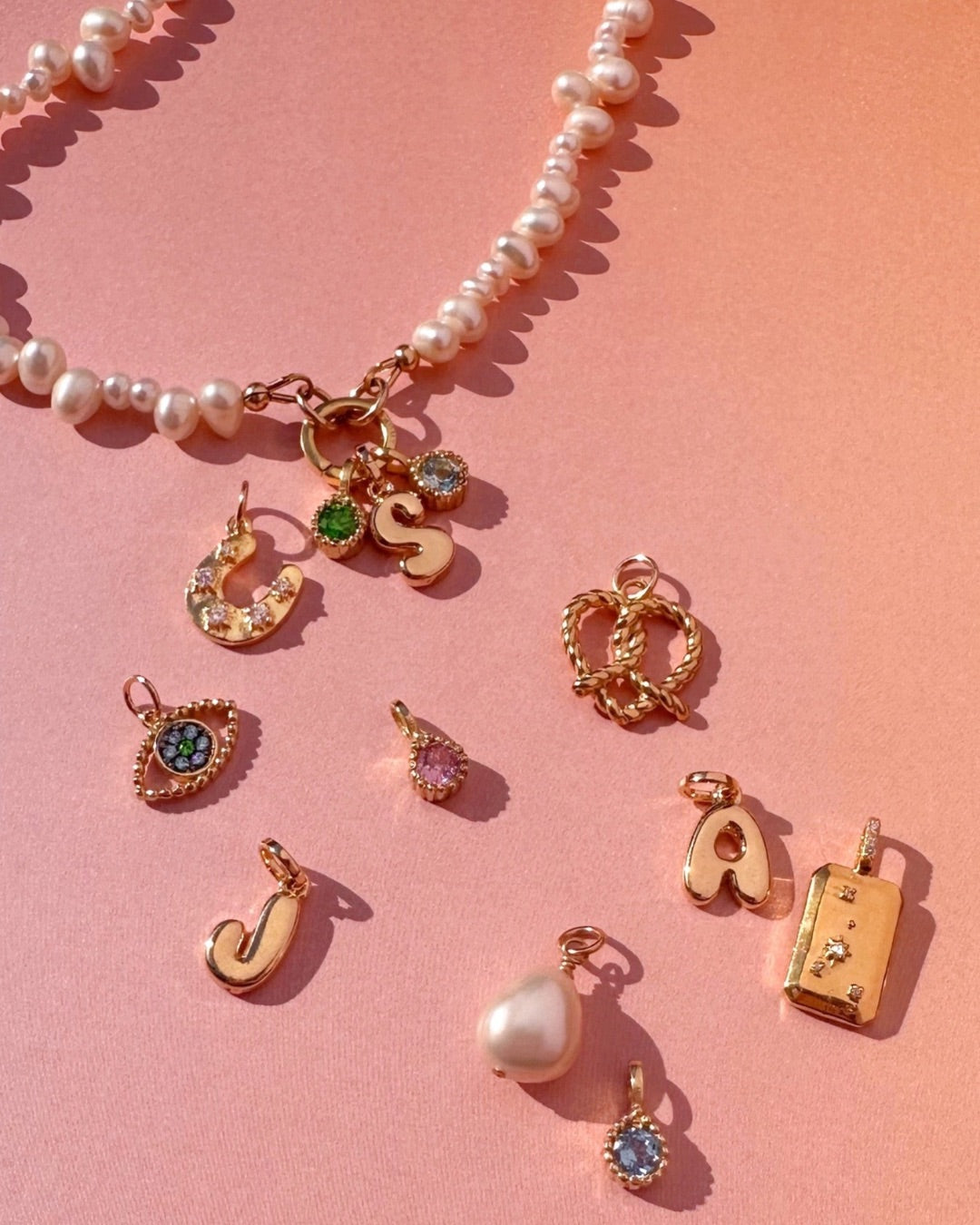 Collection of gold charms and pearl charm holder necklace on a pink background