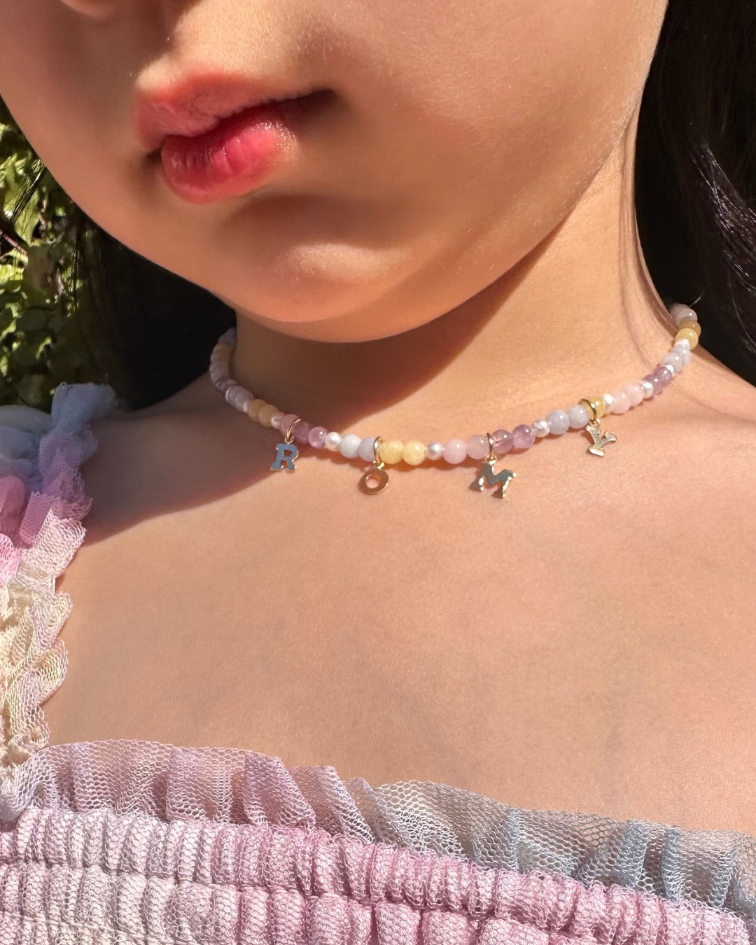 Close-up of a child wearing a colorful pastel gemstone charm necklace with a blurred background