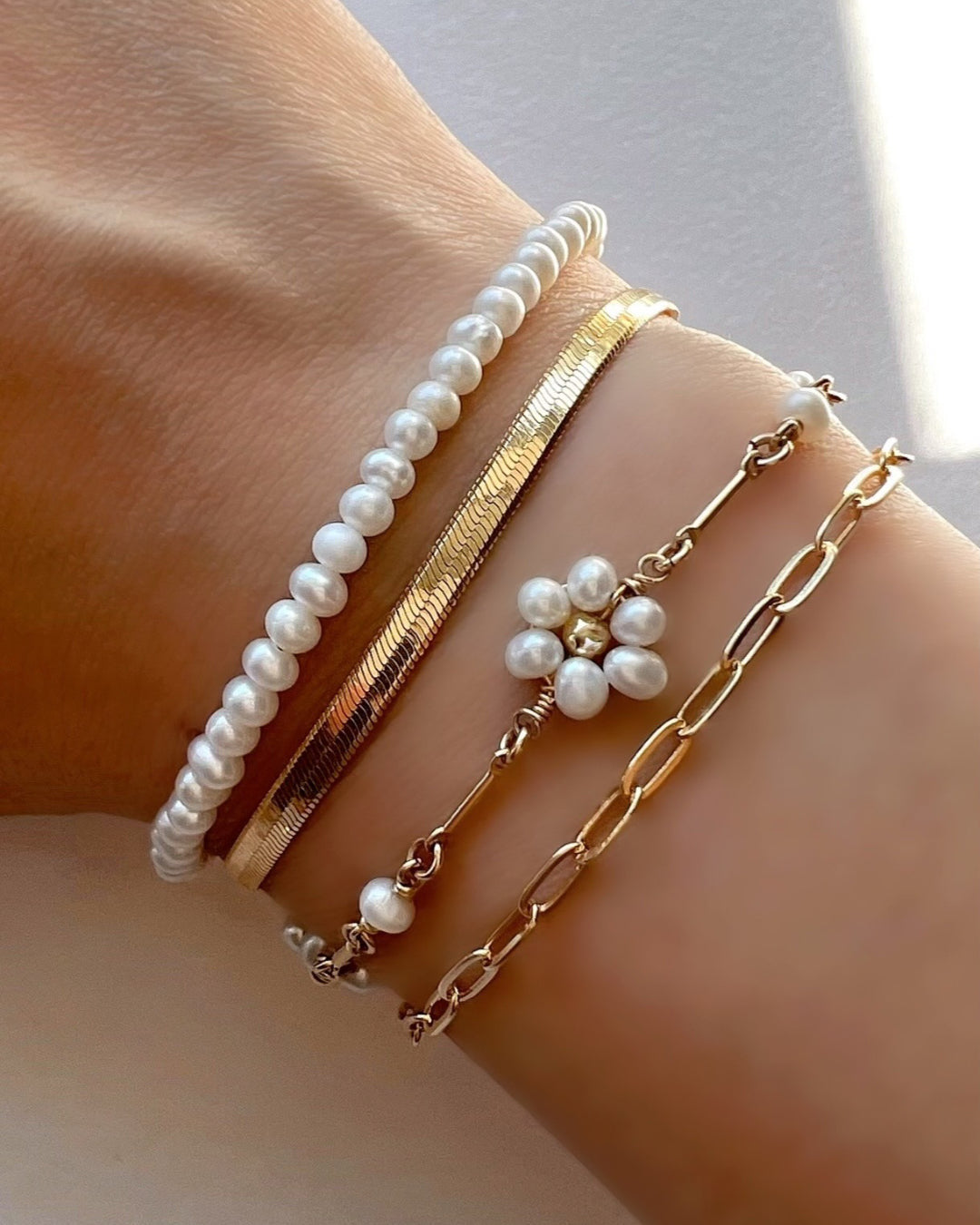 A close-up of the Daisy Pearl Bracelet Set, showcasing a delicate pearl bracelet paired with a sleek paperclip chain bracelet, stacked together for a stylish and charming look.
