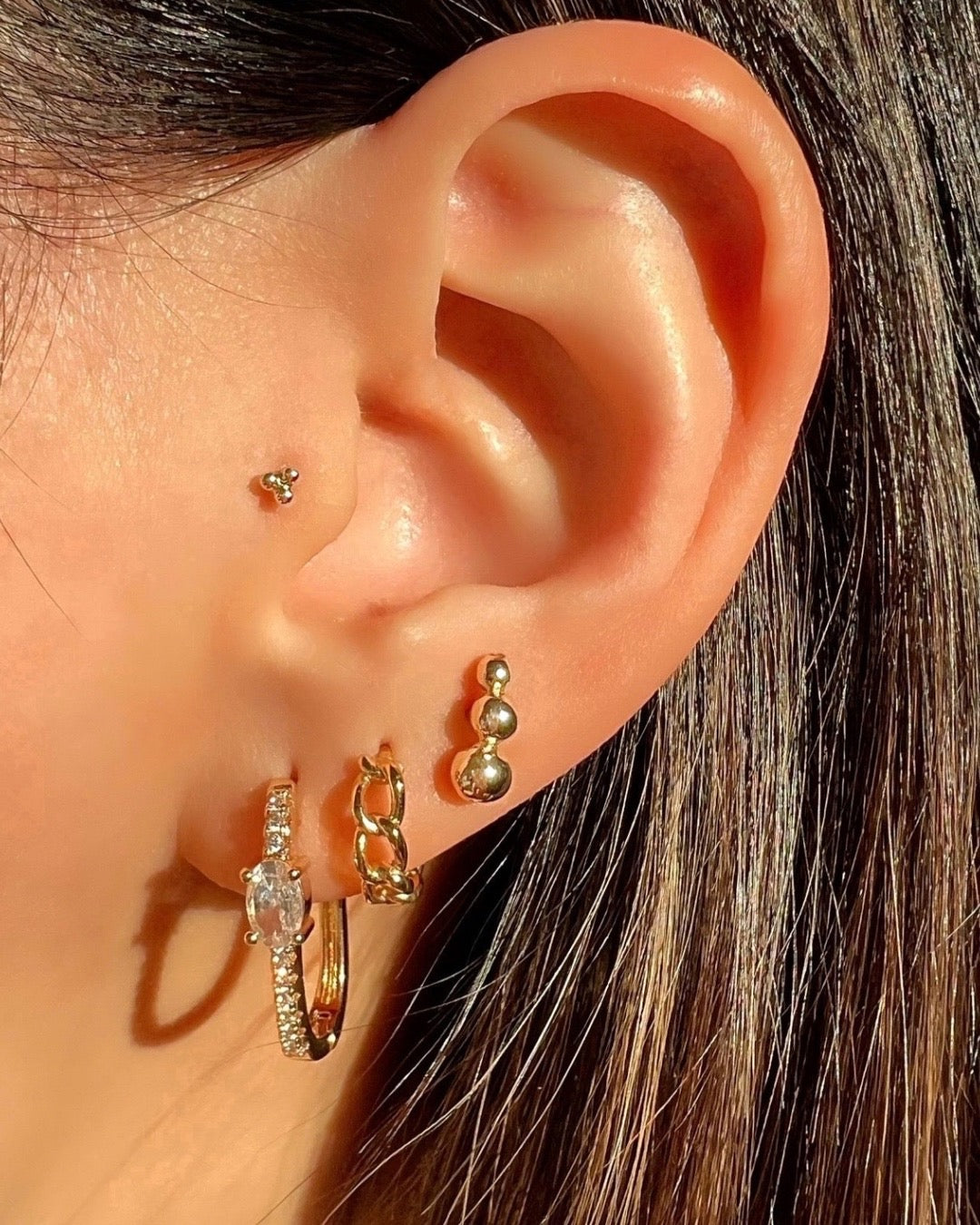 Gold cubic zirconia square pave hoop earrings stacked with gold hoop earrings and diamond stud earrings and Flatback earrings on a model