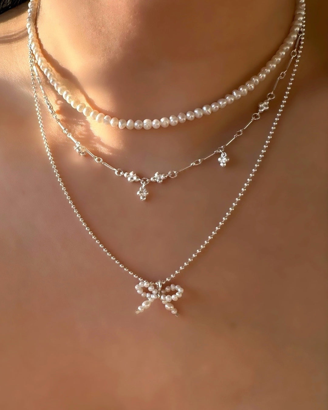 Sterling Silver Pearl Bow Pendant on a Silver necklace layered with pearl choker and Trinity Mini Spheres Ball Choker Necklace on a model