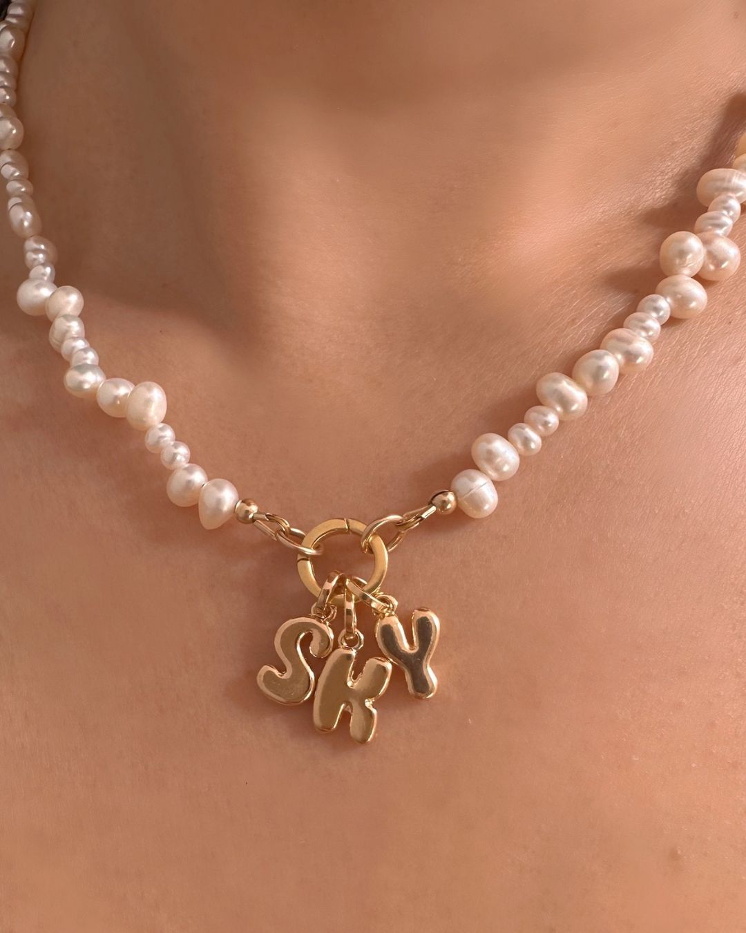 Pearl necklace with gold bubble initials 'SKY' charm on a person's neck