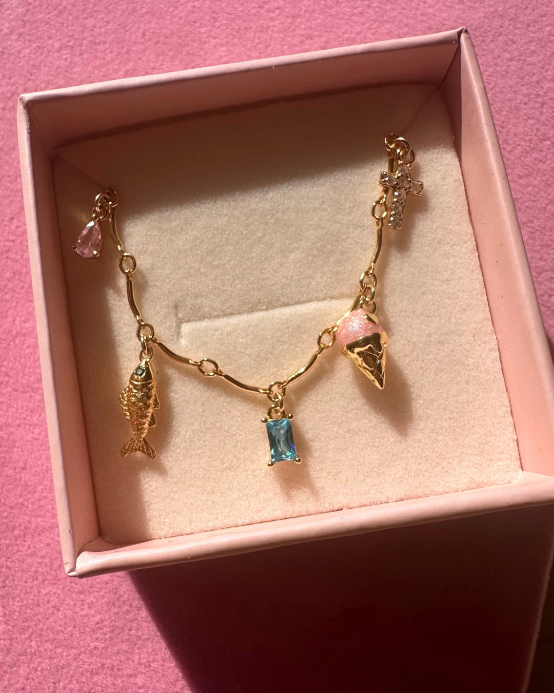 Gold charm bracelet with charms in a pink Romyli box on a pink background