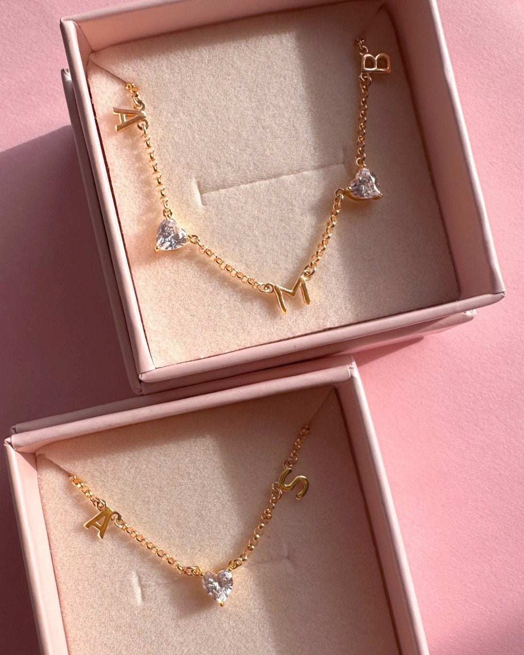 Two Petite Initial Necklaces in Romyli gift boxes — one with two gold letters and a heart gem in the centre, the other with three gold letters and two heart gems interspacing, 14k gold fill personalised jewellery from Australia