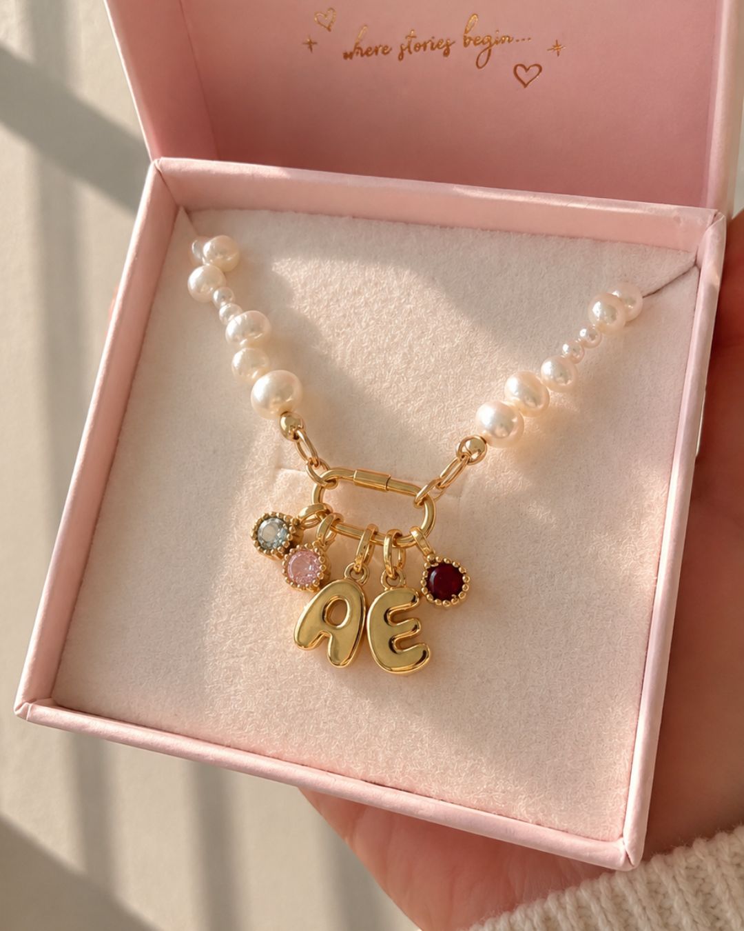 Pearl necklace with gold bubble initial charms and birthstone pendants in a pink jewelry box.