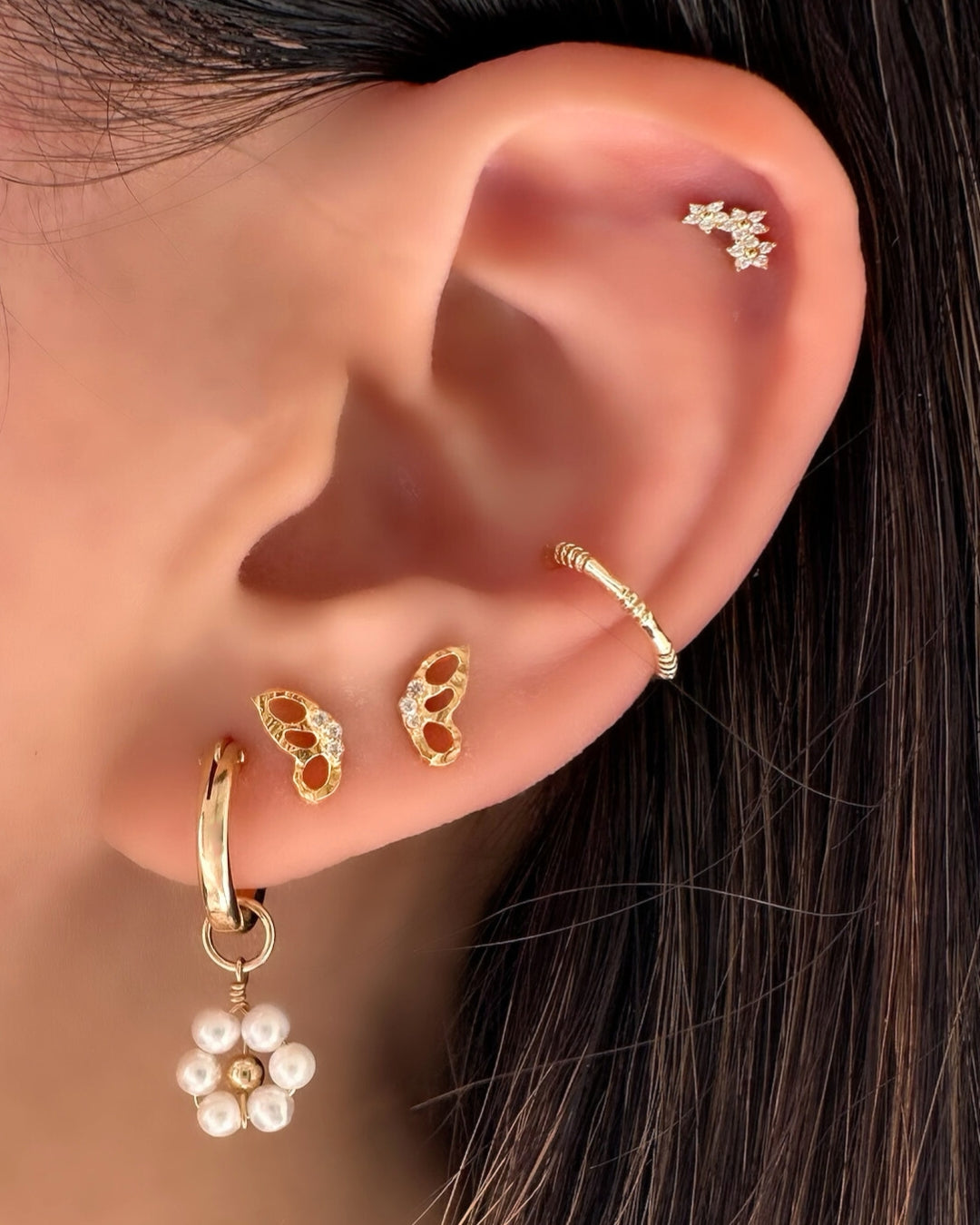 Daisy Pearl Charm Hoops stacked with Butterfly Flutter Studs, Divinity Ear Cuff and Trilia Reversible Stud on a model