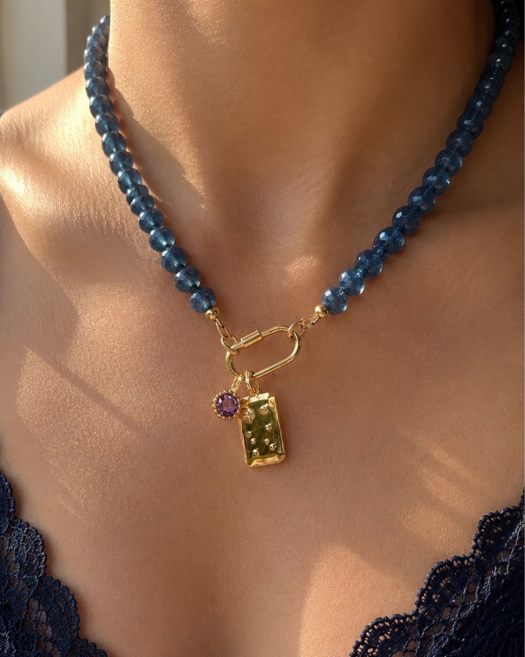 Dusk Charm Holder Necklace with blue beads and a gold clasp and Constellation and Birthstone charms on a person wearing a navy blue lace top.