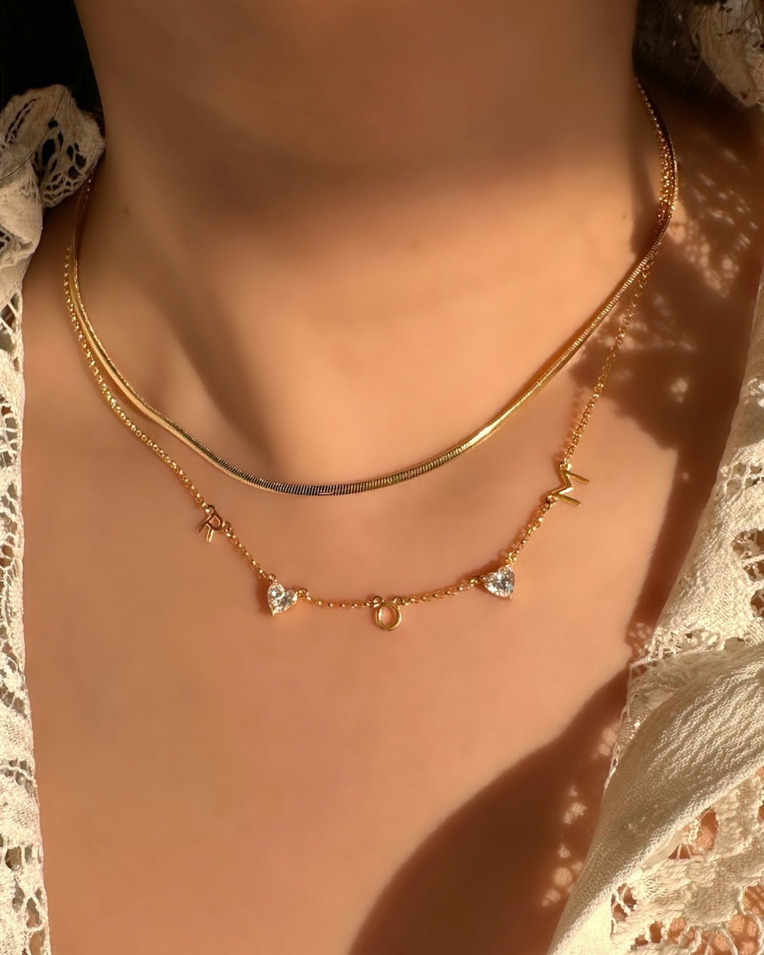 Model wearing custom gold-filled necklace with 3 initial letter charms and 2 heart gems evenly spaced on a petite rolo chain.