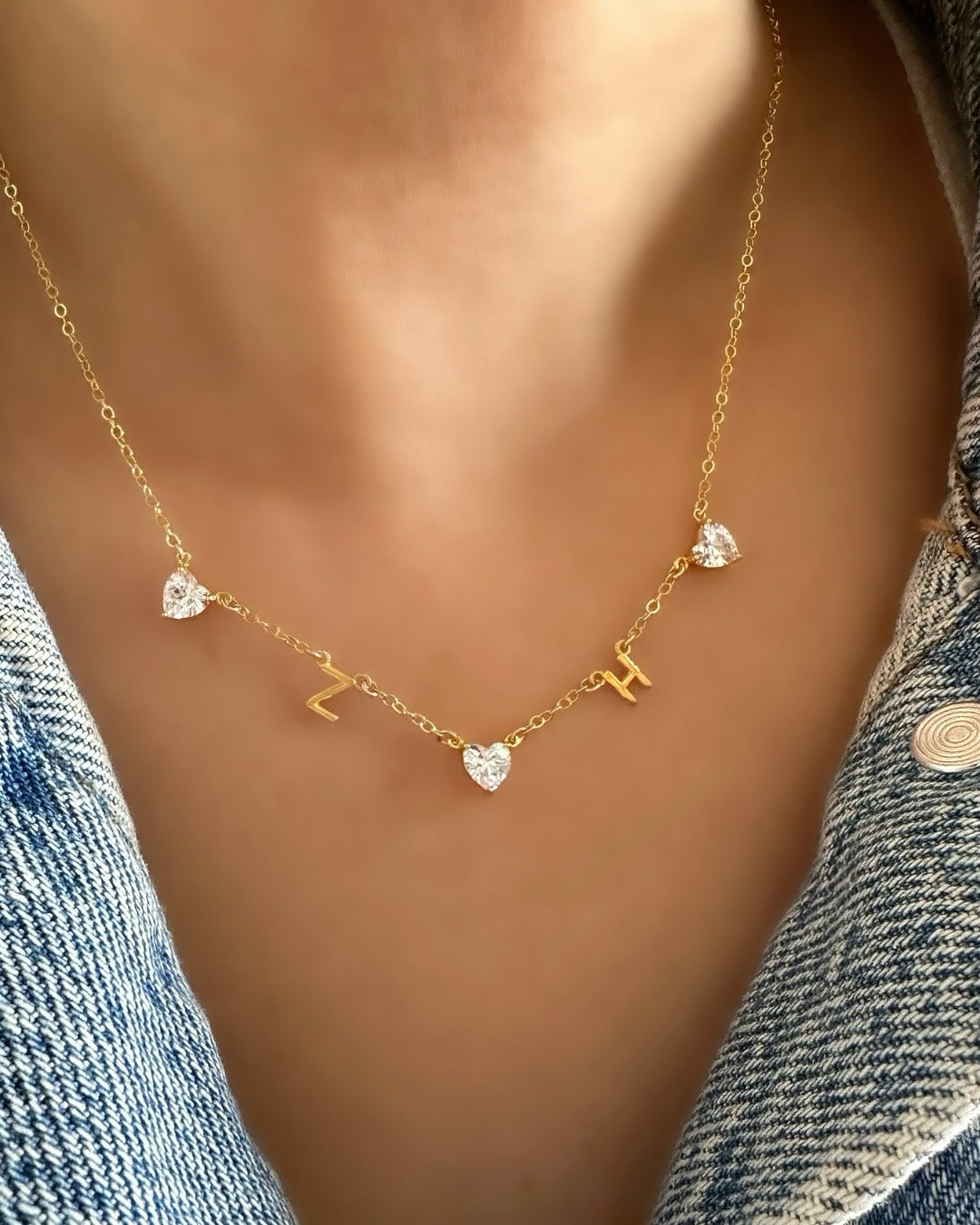 Model wearing customisable gold-filled necklace featuring a mix of letter charms, heart gem charms on a petite rolo chain