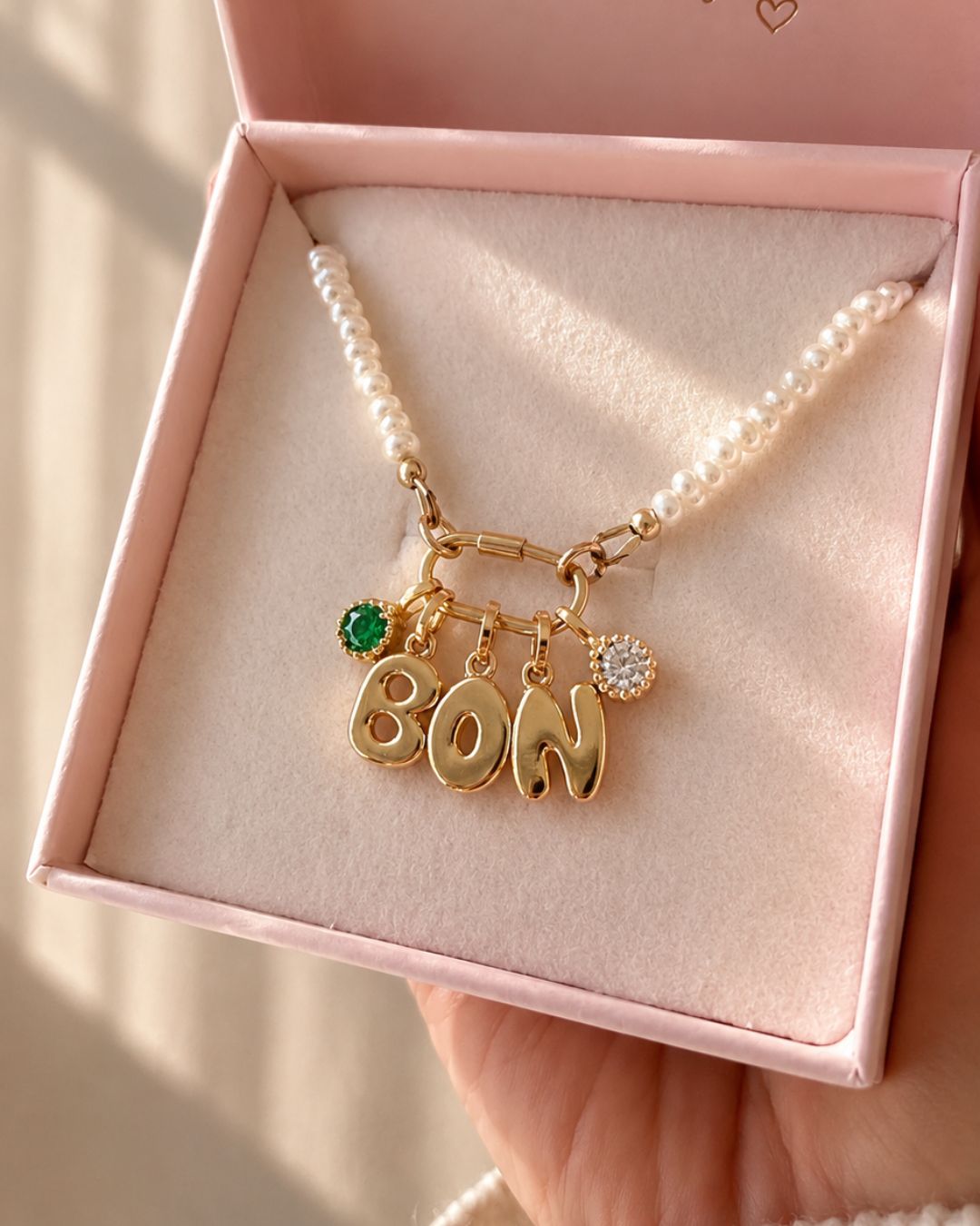 Gold necklace with bubble initial charms and birthstone pendants in a pink jewelry box
