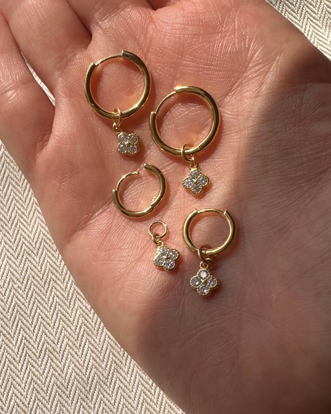 Gold Mini Clover Charm Hoops in small and medium size on a hand