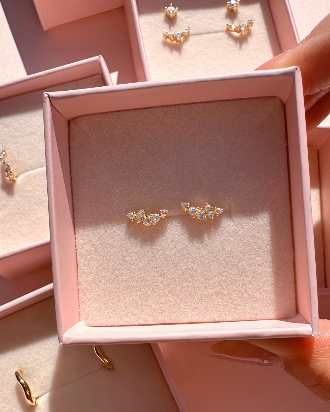 Gold climber stud earrings with a curved linear cluster of brilliant round crystals in a Romyli jewellery box